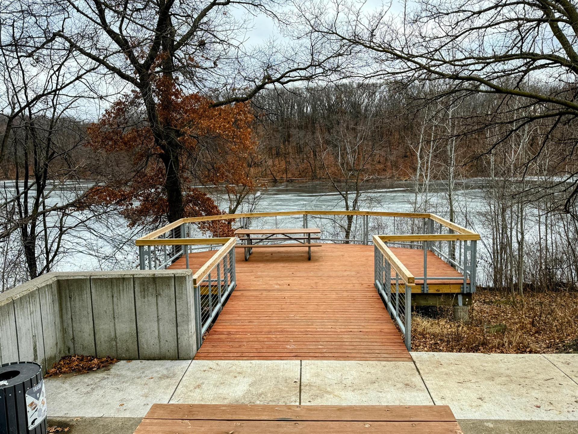 Wooden observation deck with a picnic table overlooking a partially frozen river.