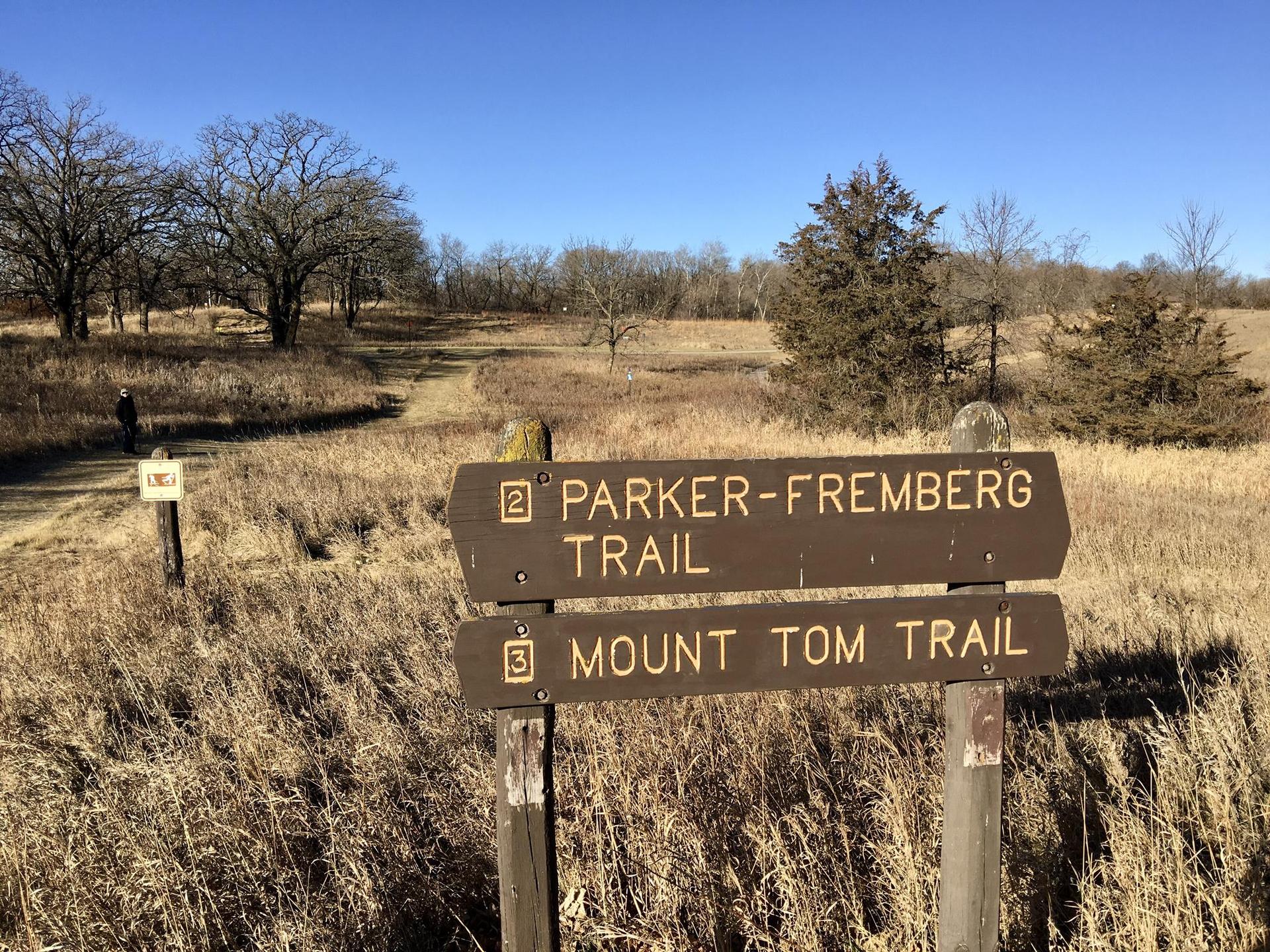 Wooden trail sign in a dry grassy field under a clear blue sky.