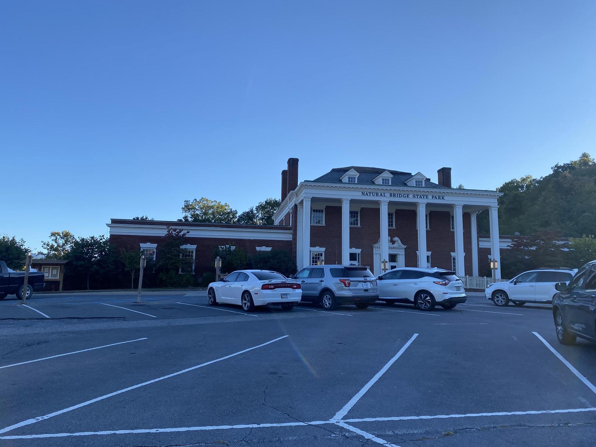 Large building with white columns and a parking lot under blue sky.