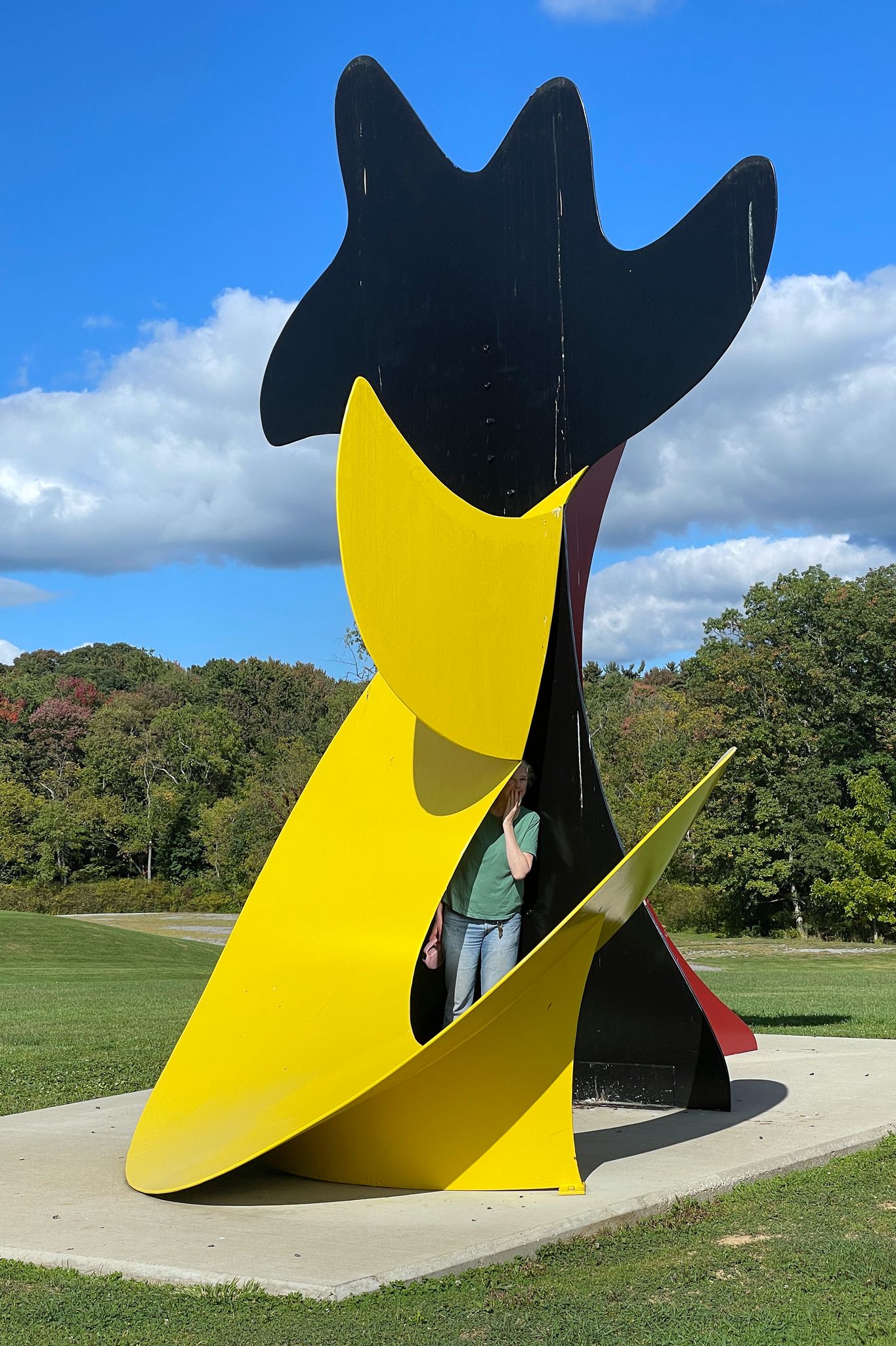 A person stands inside a large, colorful abstract sculpture on a sunny day. - Large Escargot sculpture – Manly Sculpture by Lyman Kipp loop from Browns Woods