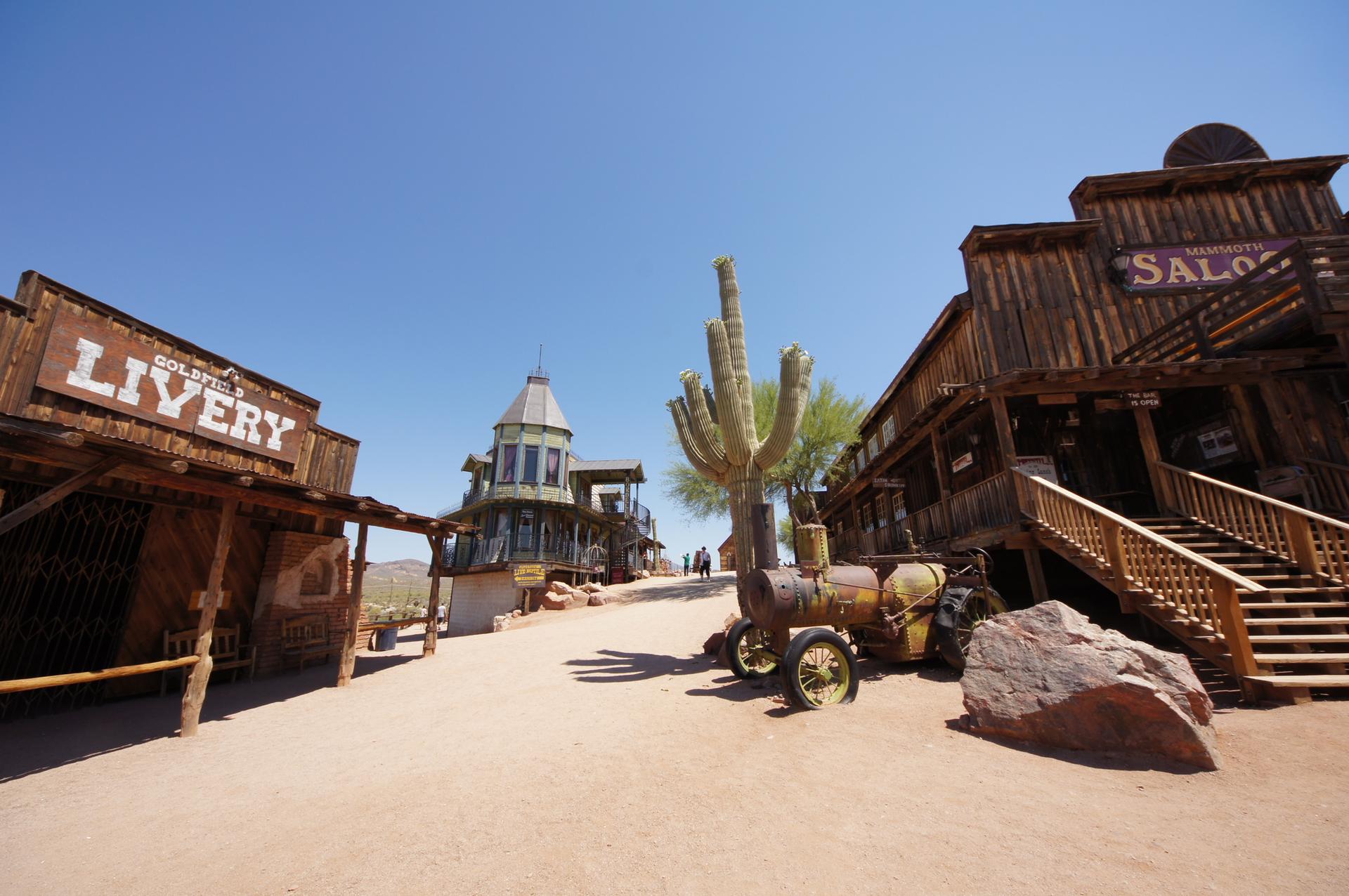 Old Western town street with wooden buildings, a saguaro cactus, and clear sky.