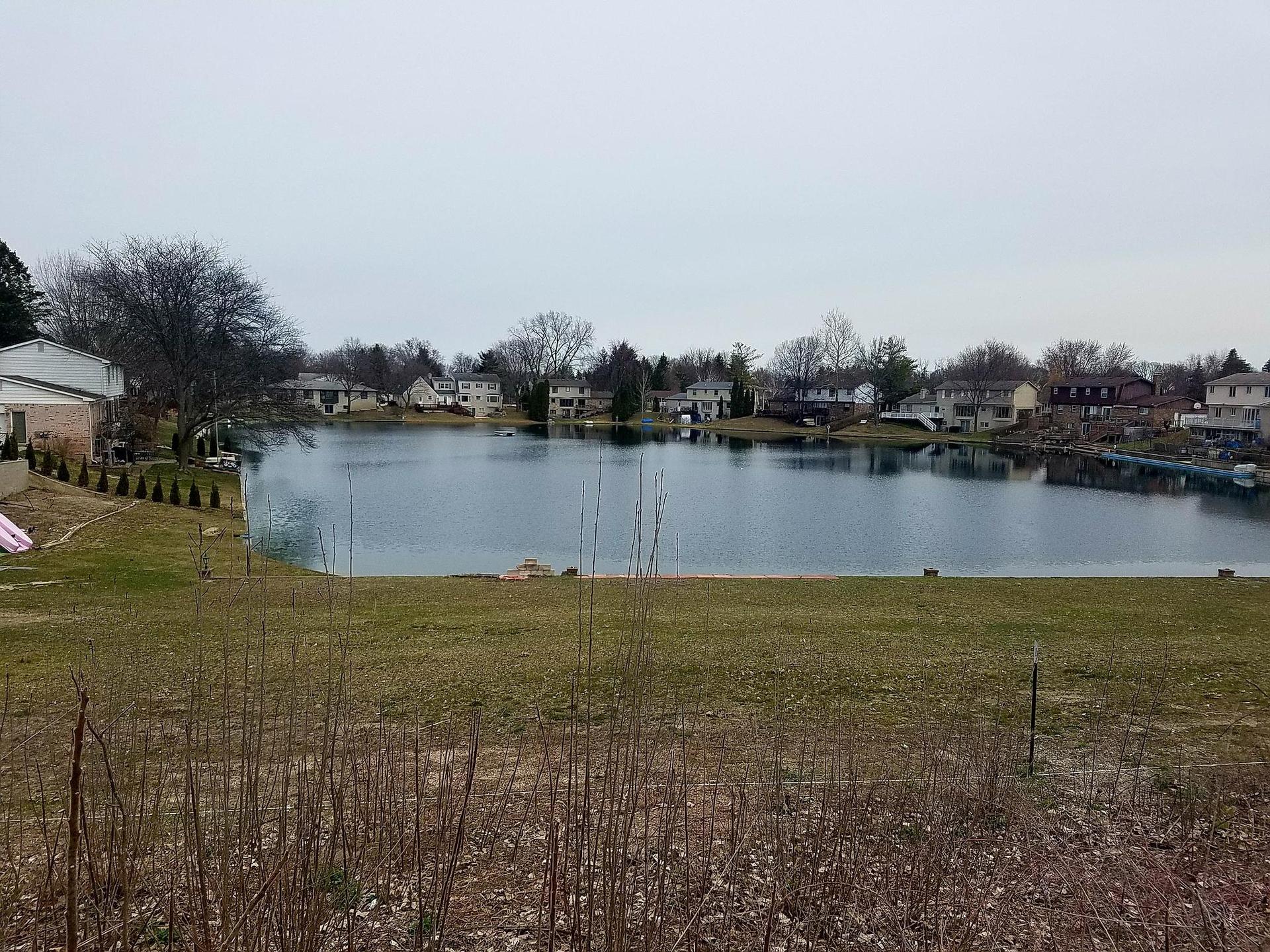 A large lake surrounded by houses and green lawns under a gray sky.