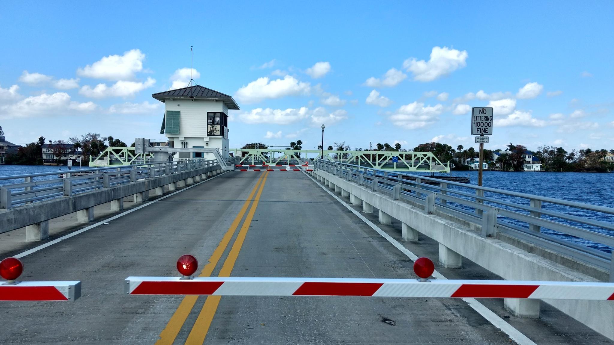 Closed drawbridge with barriers and a bridge house under a blue sky.