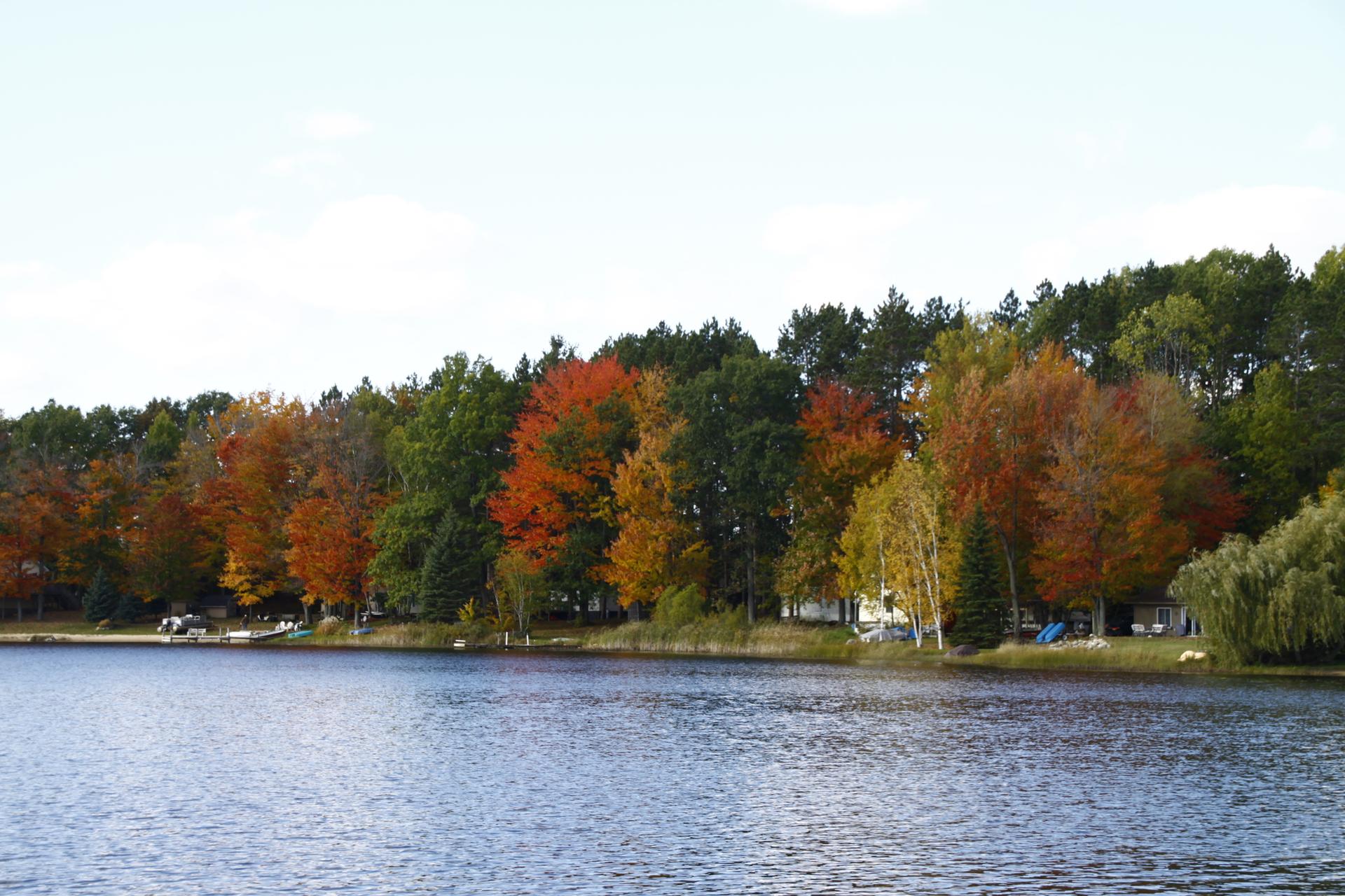 Lake reflecting vibrant autumn trees under a bright sky.