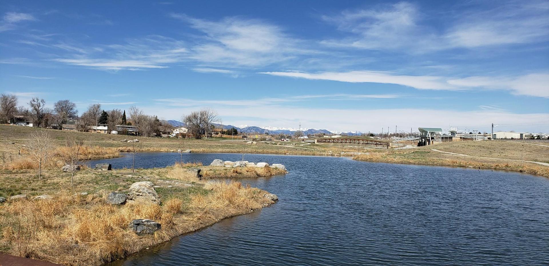 A pond with dry grassy banks under a bright blue sky with distant mountains.