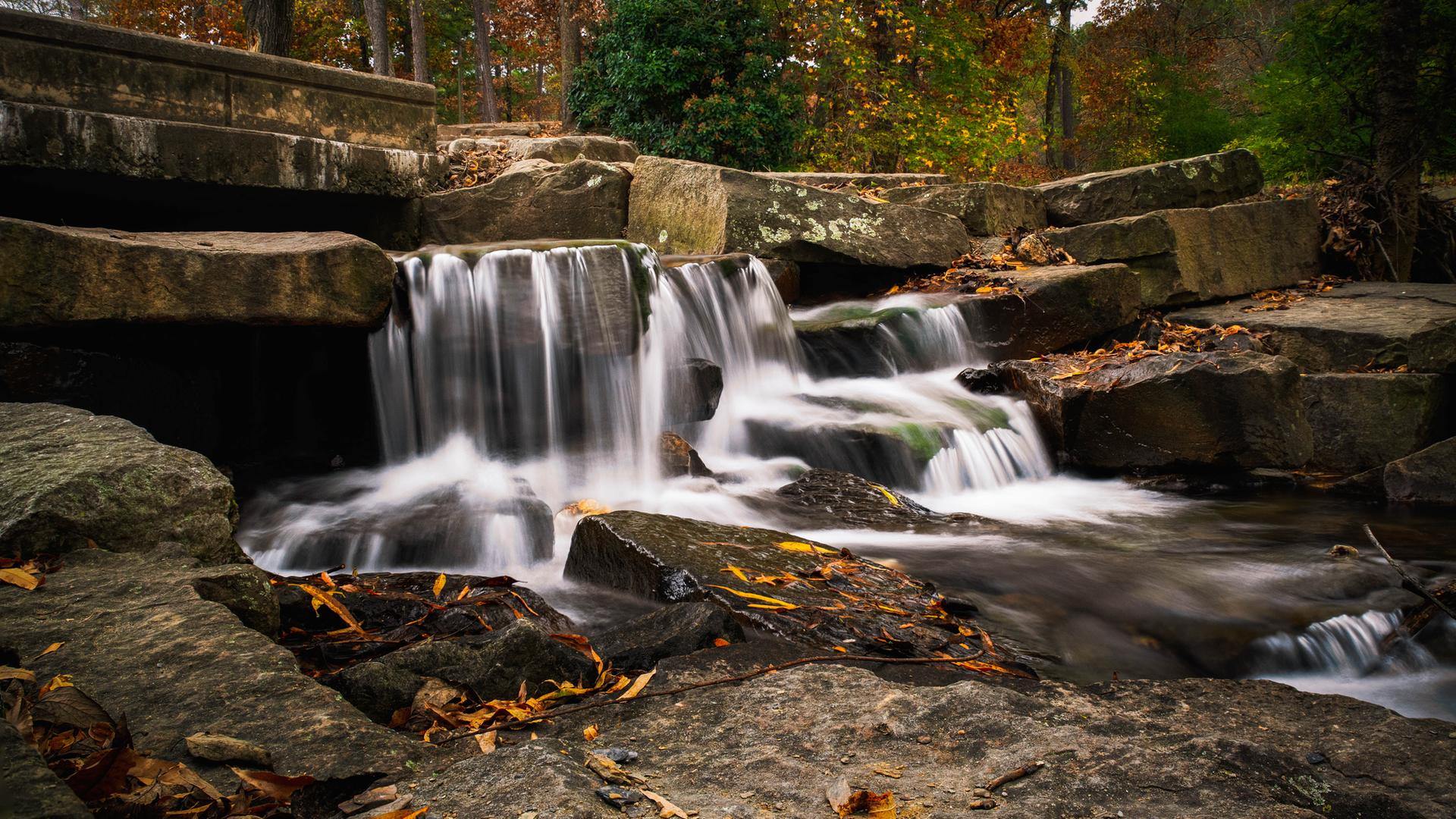 Silky waterfall cascades over large rocks in a vibrant autumn forest.