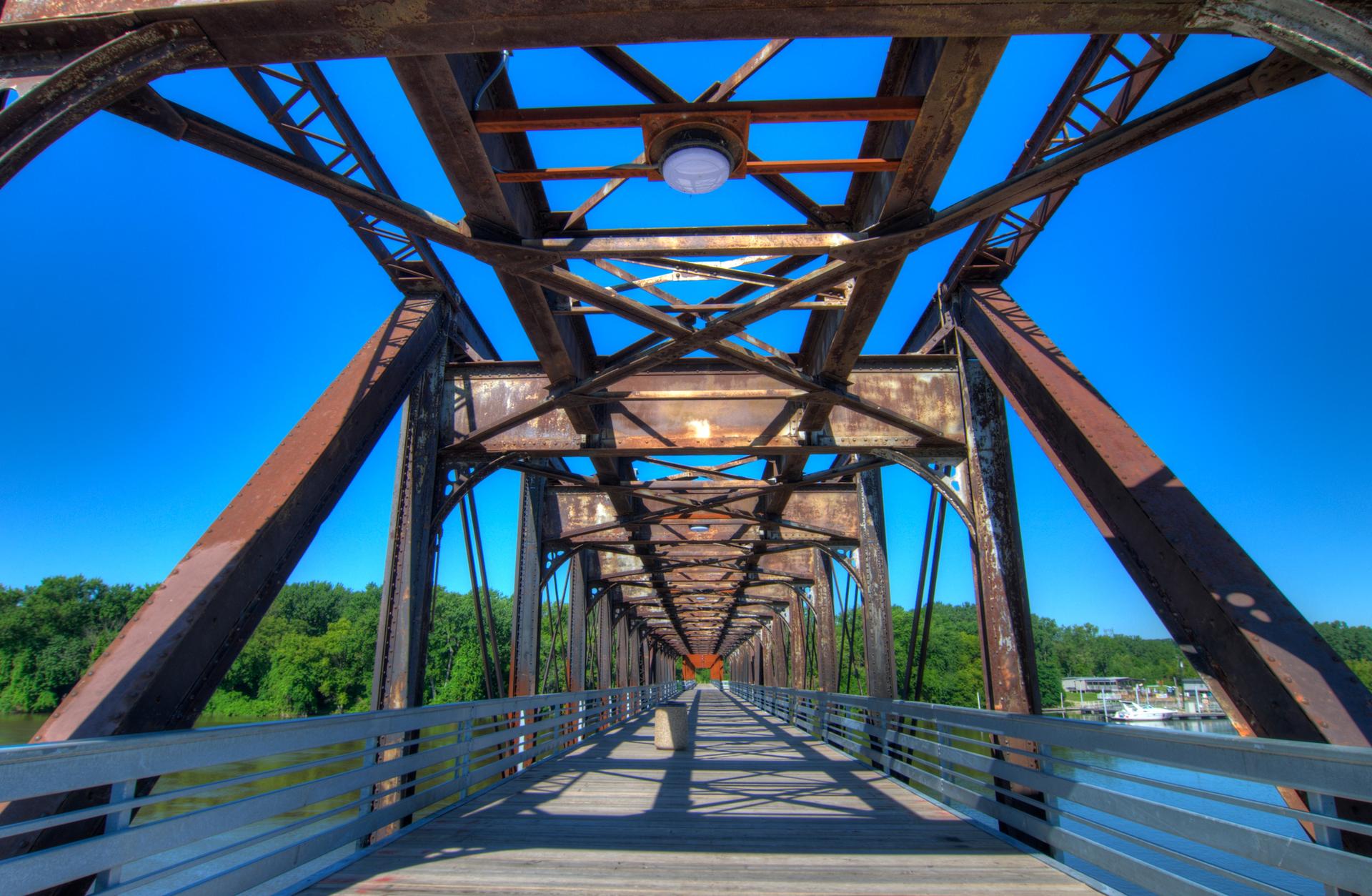 Looking up through the rusty metal structure of a long bridge.