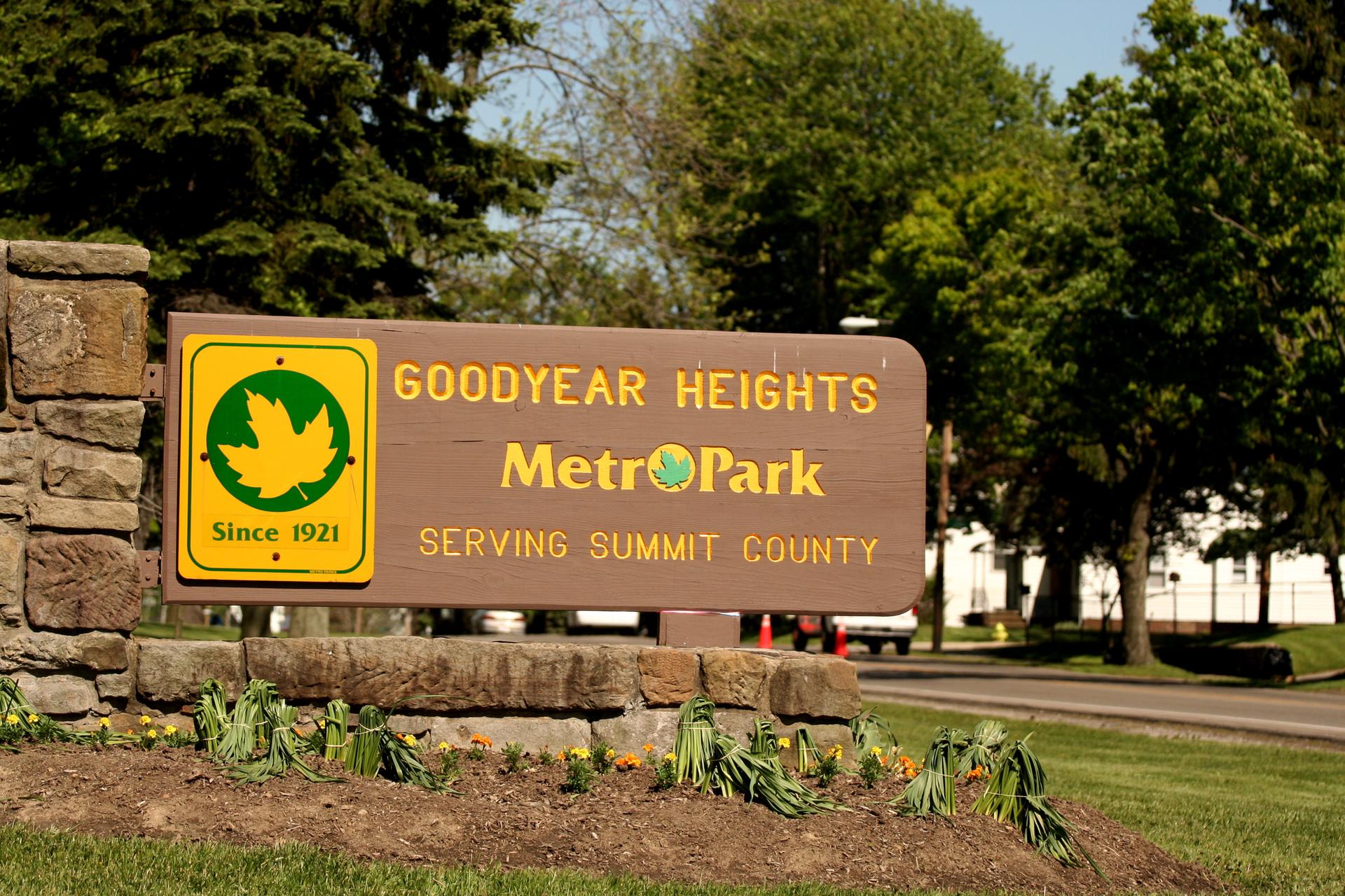 A brown wooden sign with a green logo on a stone base, sunny day.