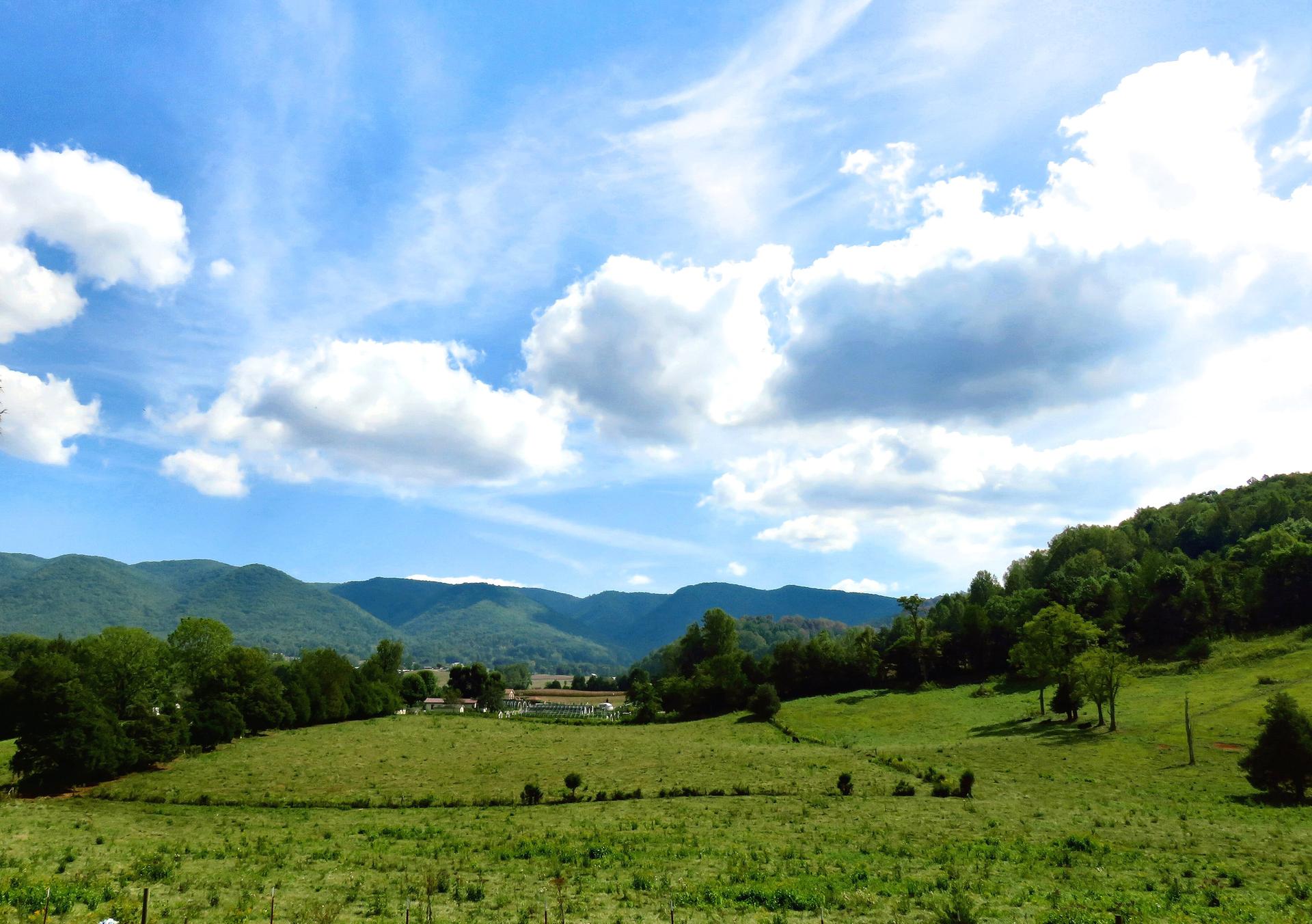 Vast green fields and forested mountains under a bright, cloudy sky.