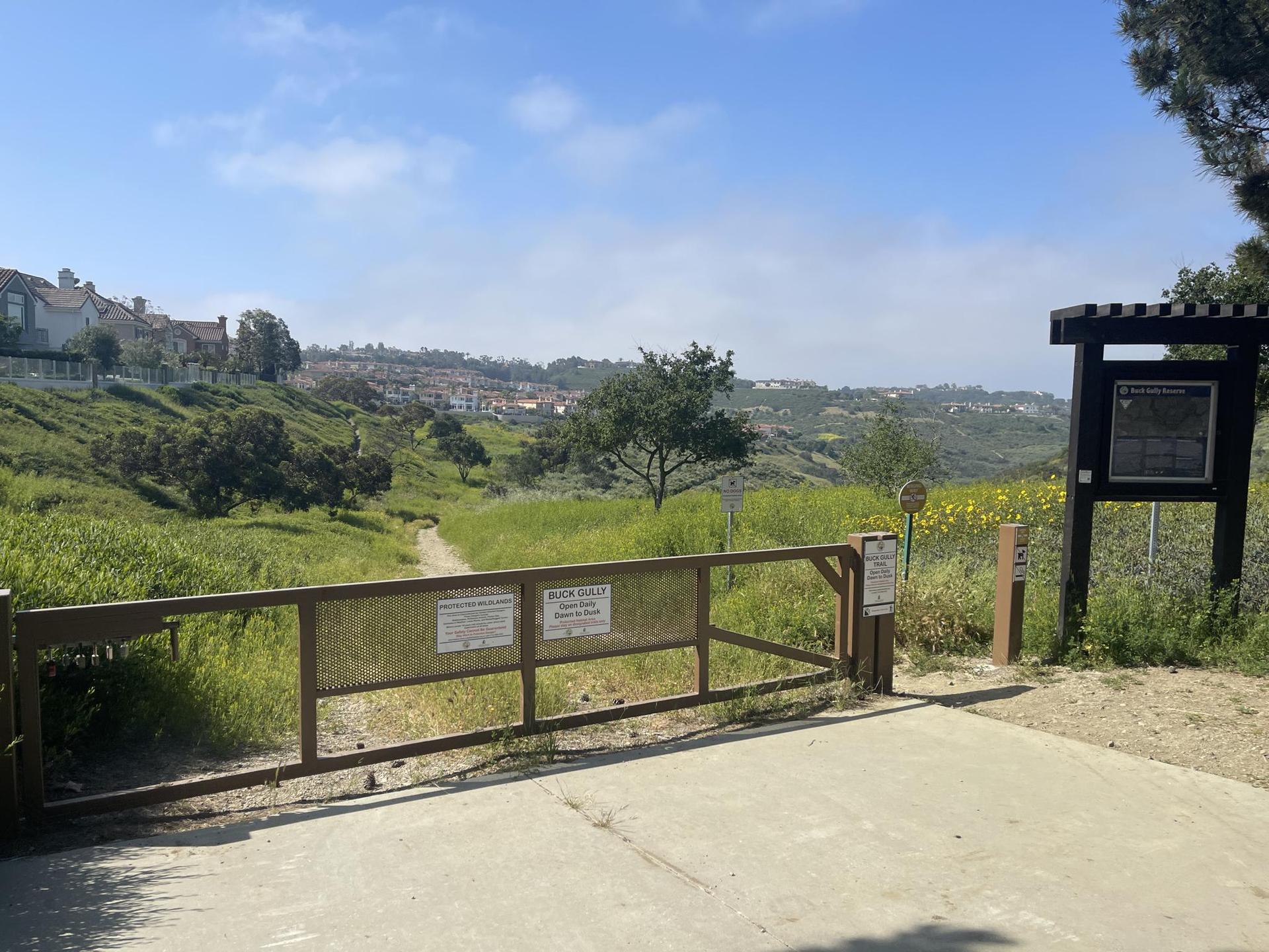 Wooden gate and sign at a trail entrance, leading to a grassy field.