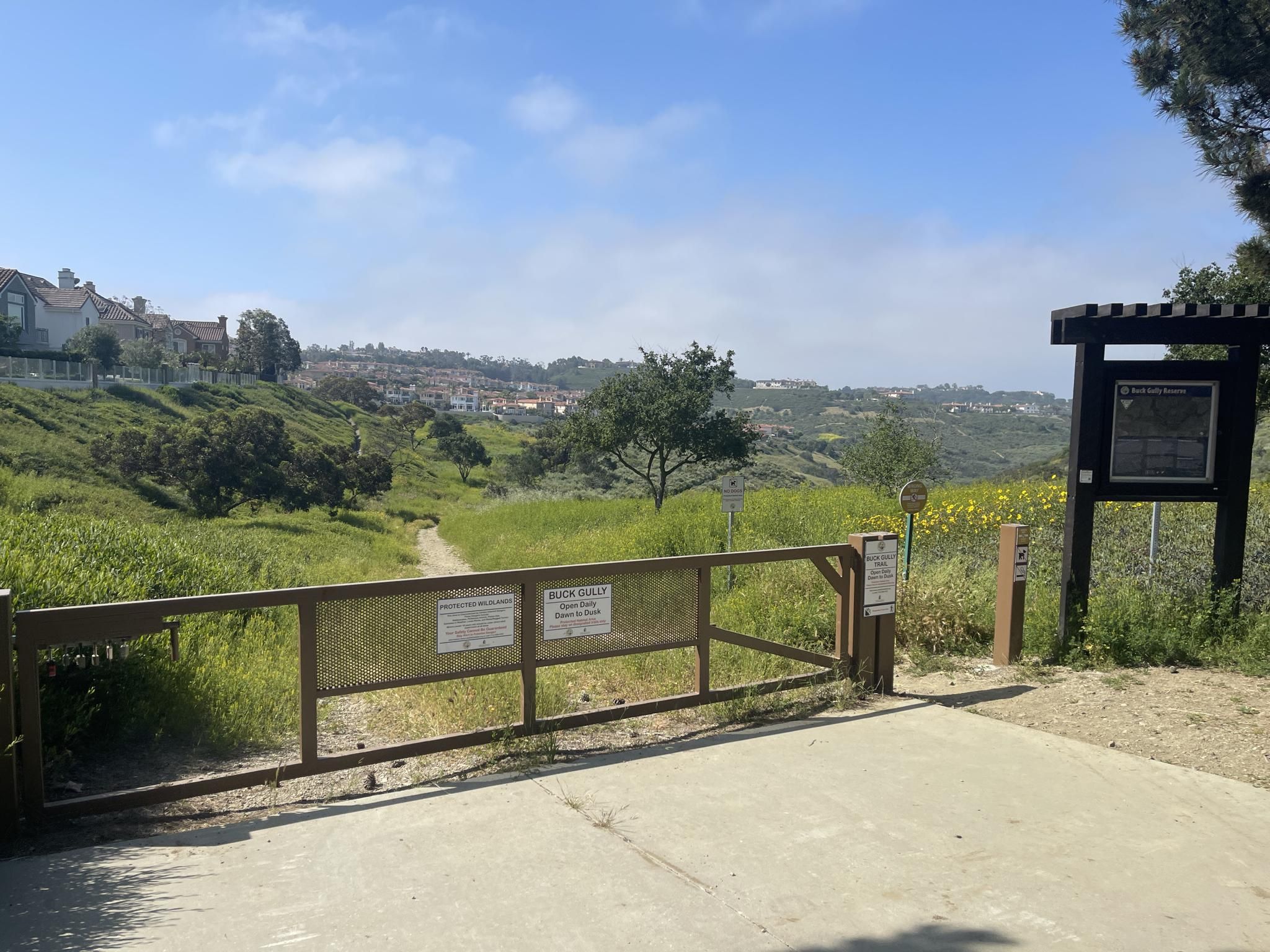 Wooden gate and sign at a trail entrance, leading to a grassy field. - Buck Gully Trailhead loop from University of California, Irvine