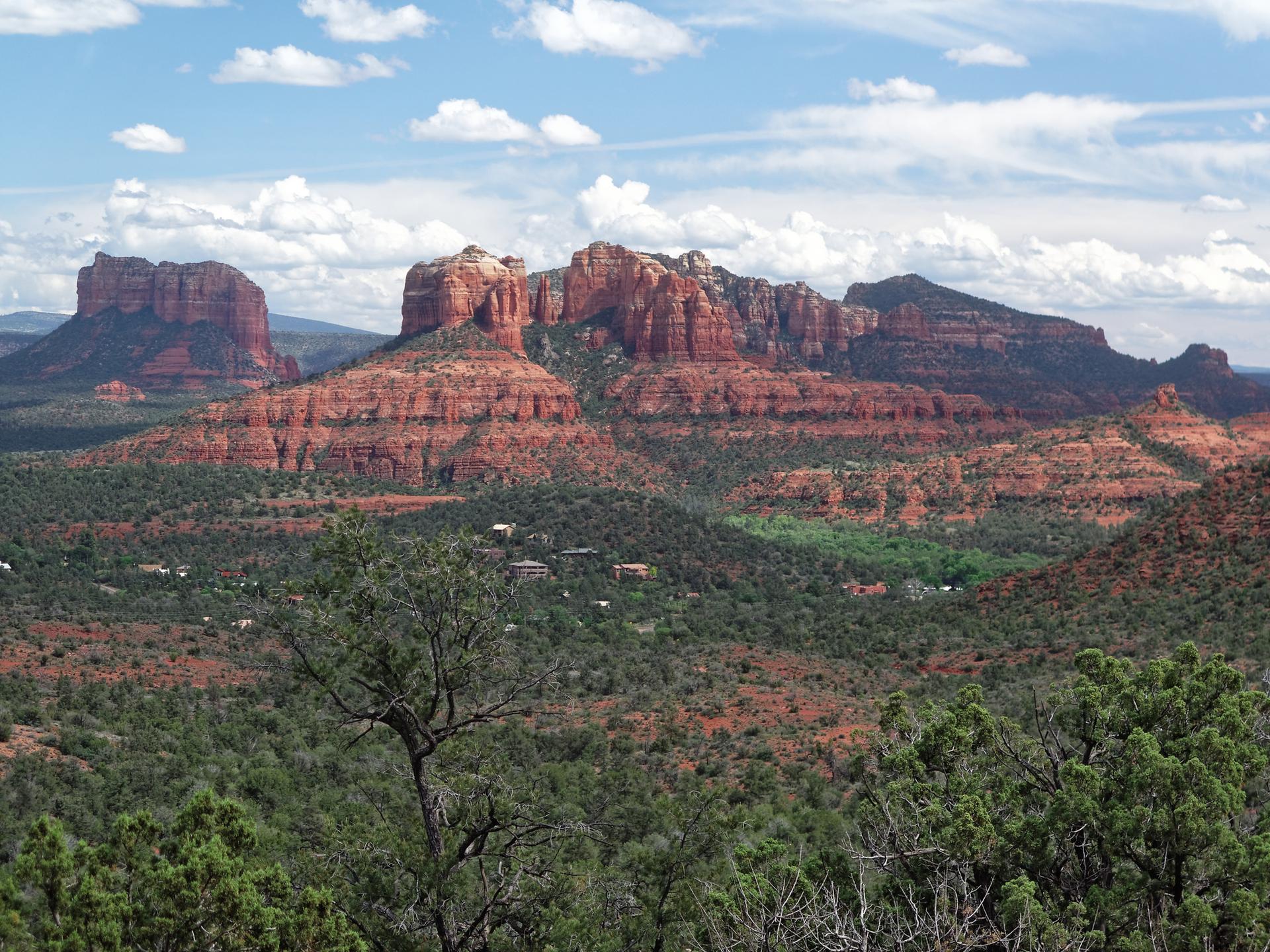 Panoramic view of majestic red rock mountains and green desert landscape under a cloudy sky.