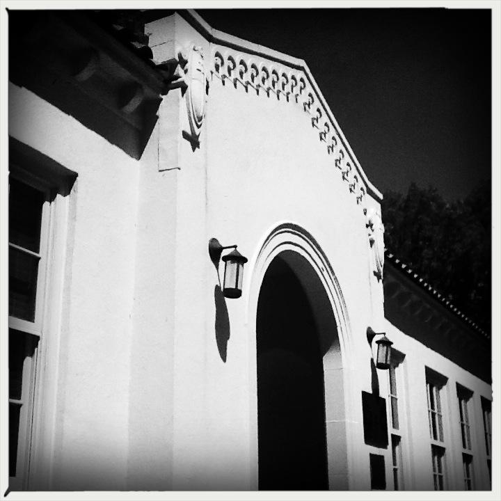 High-contrast black and white photo of a white building facade with archway and lanterns.