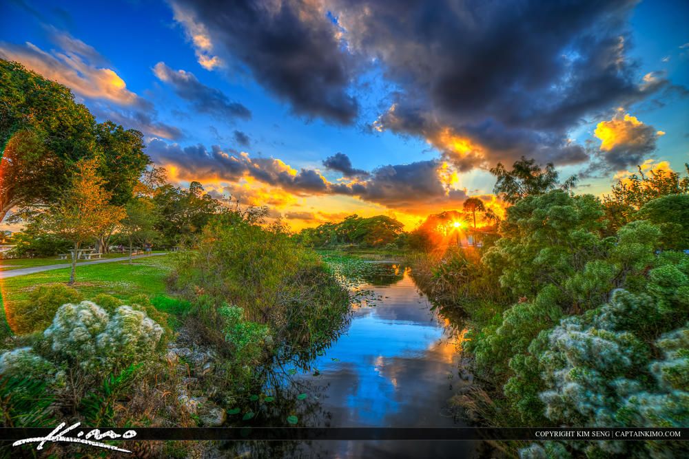 Vibrant sunset over a winding river, surrounded by lush green trees and dramatic clouds. - Lake Ida Park Loop
