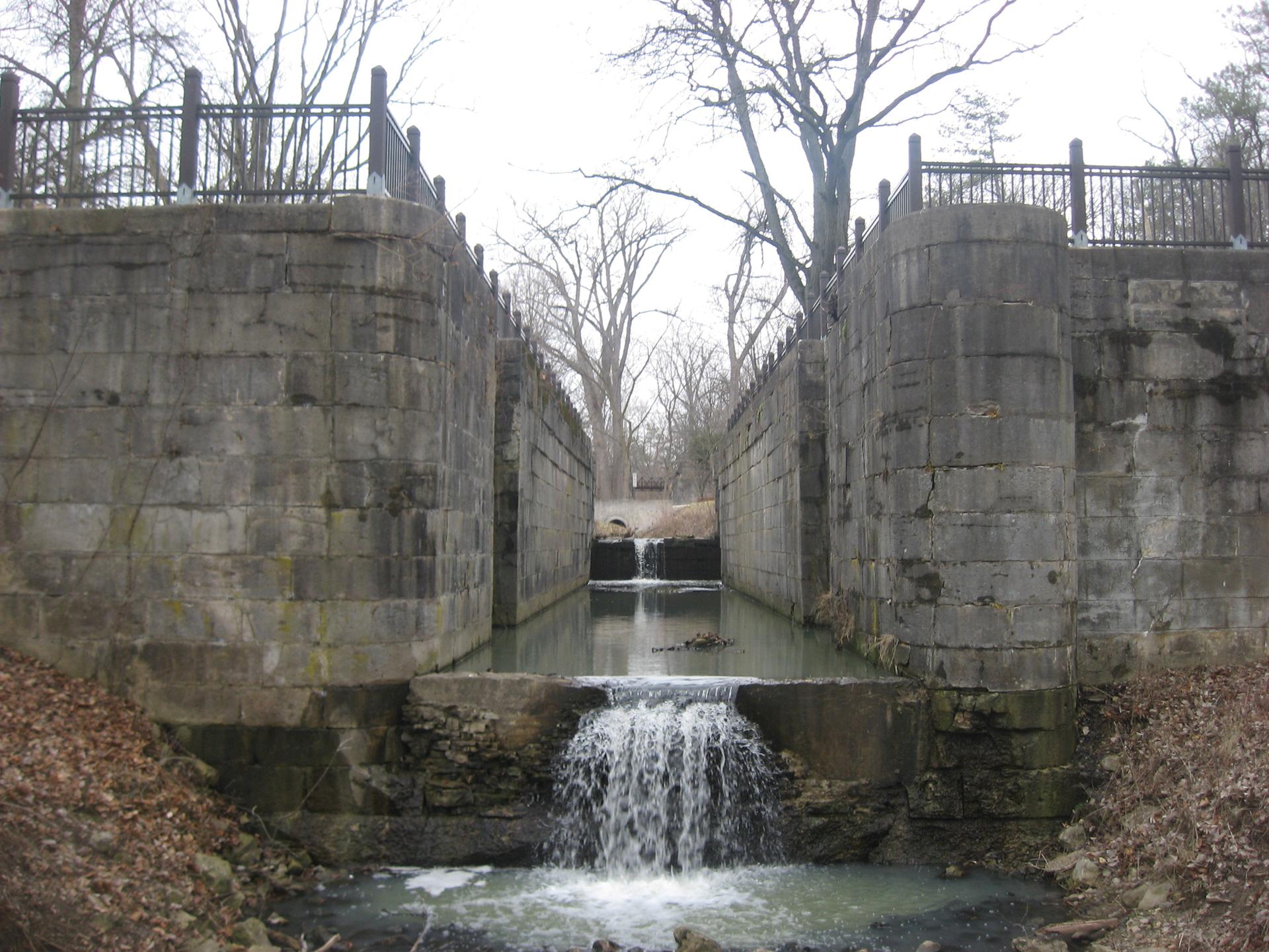 A stone canal lock with a small waterfall and bare trees.