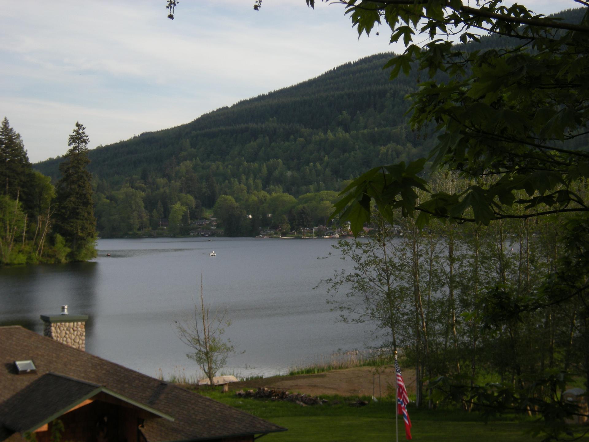 Serene lake with forested mountains and a house on the shore.
