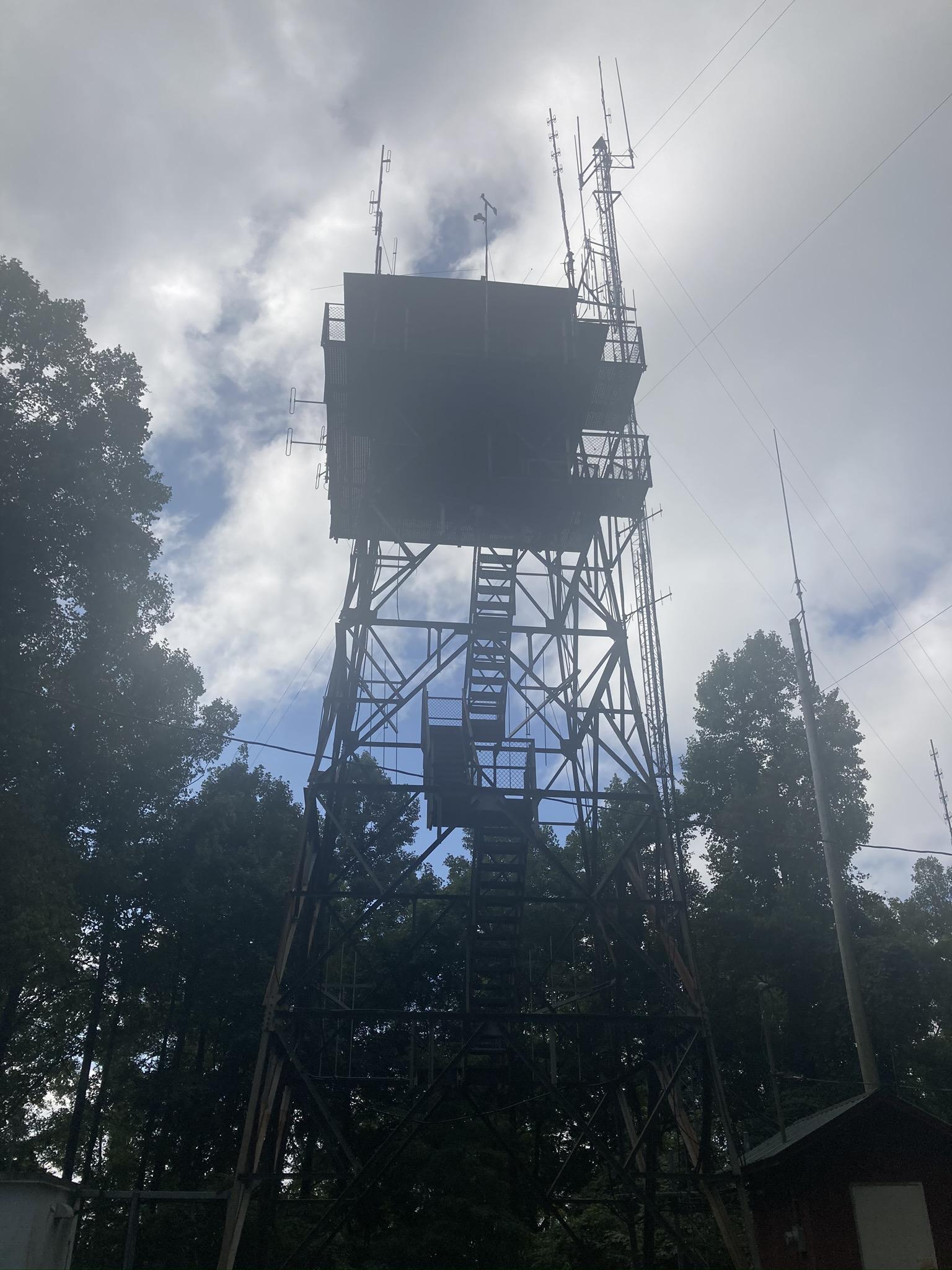 A tall metal tower with a top cabin, silhouetted against a bright, cloudy sky.