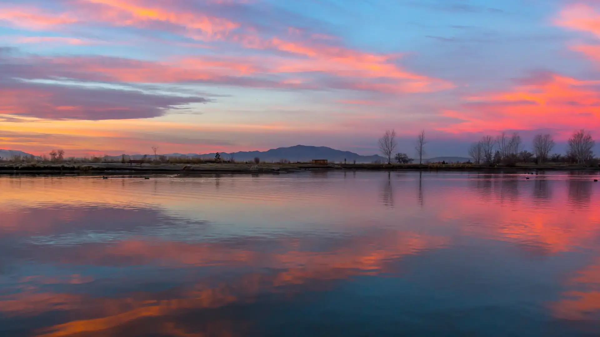 Vibrant pink and orange sunset clouds reflected perfectly in still lake water.