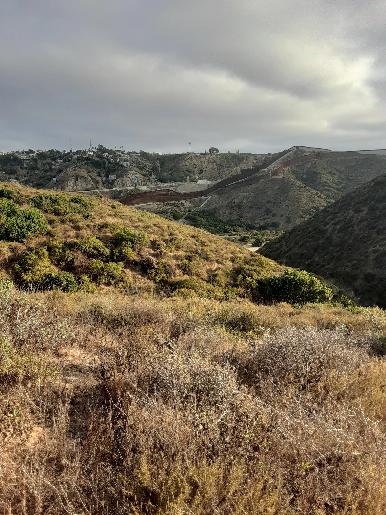 Overcast view of dry, rolling hills covered in brush and distant structures. - Spooners Mesa Trail Loop