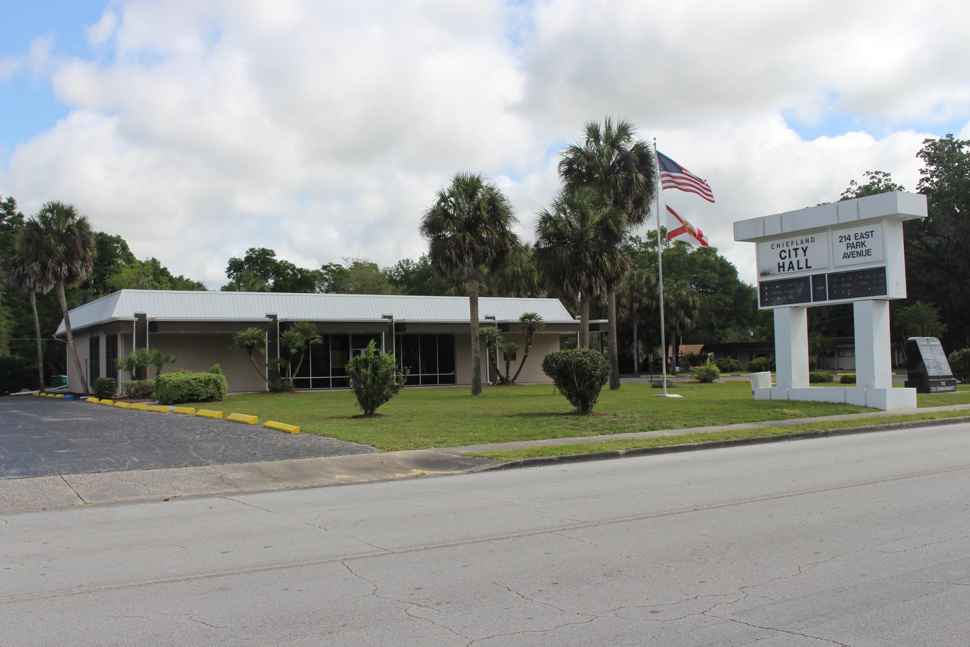A low building with a sign and flags, surrounded by palm trees.