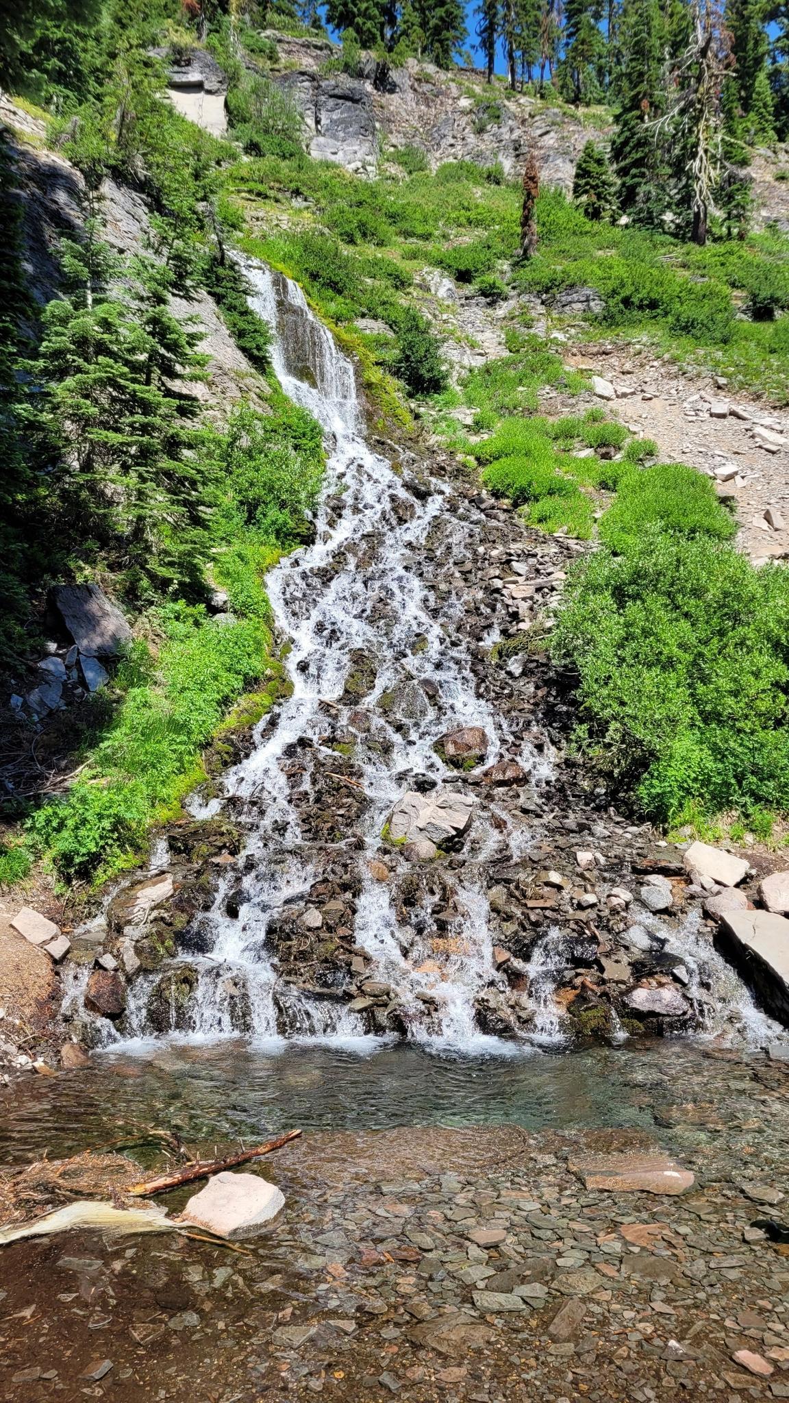 Waterfall cascades over rocks into a clear pool on a sunny day.