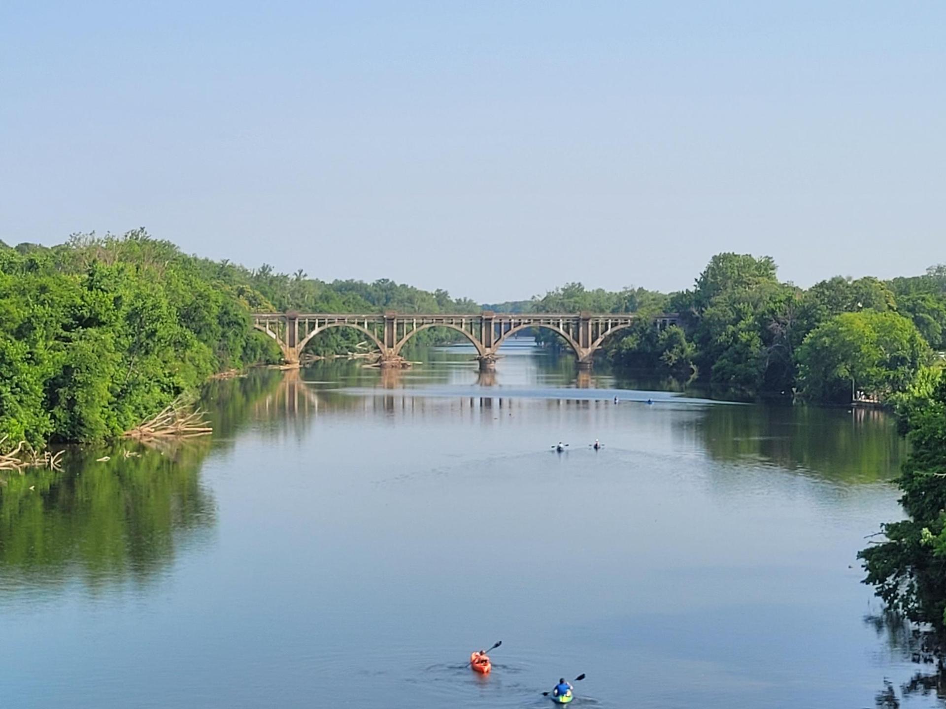 Kayakers on a wide river under an arched bridge on a clear day.