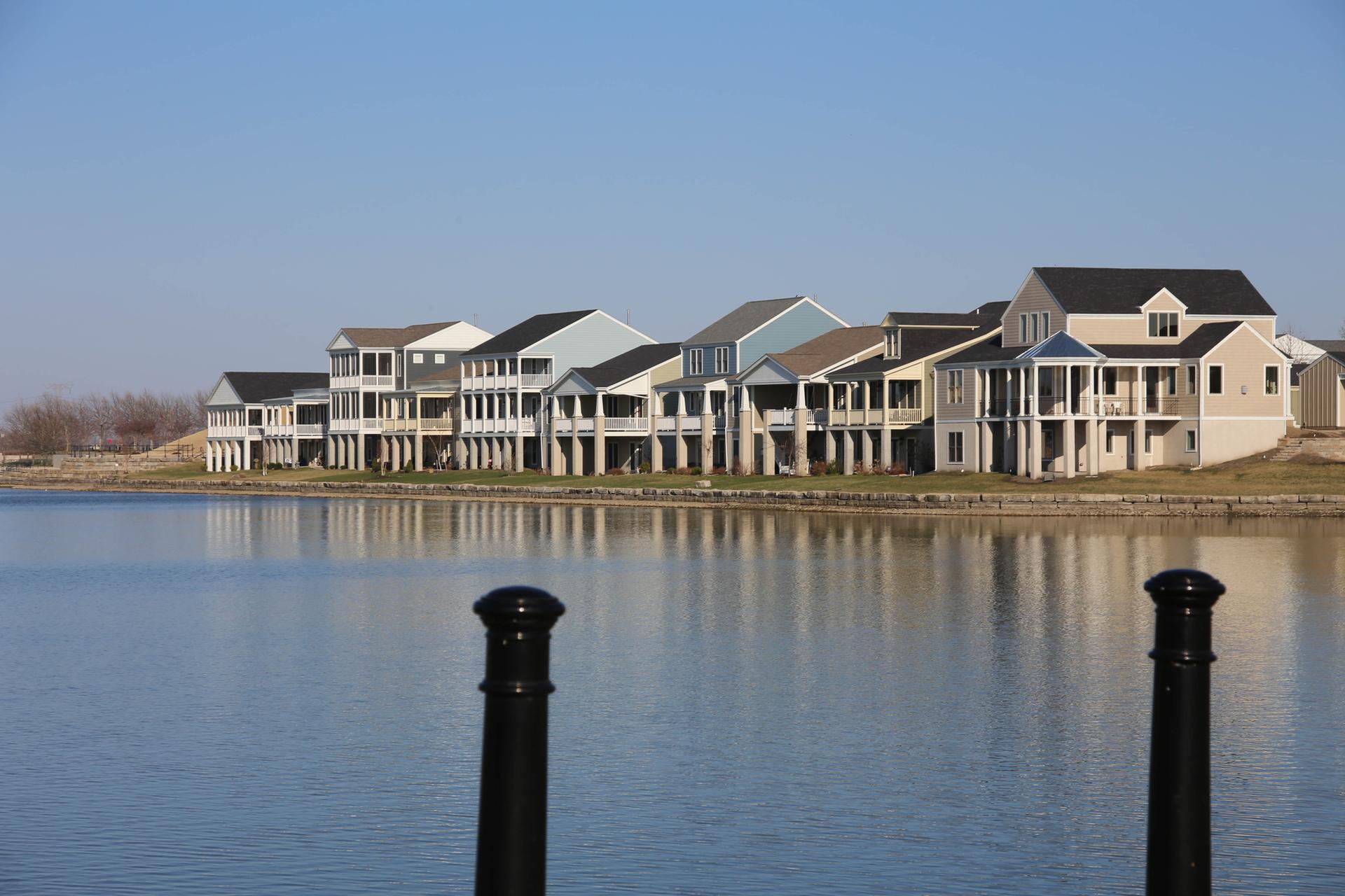 Modern waterfront houses with balconies line a calm body of water.