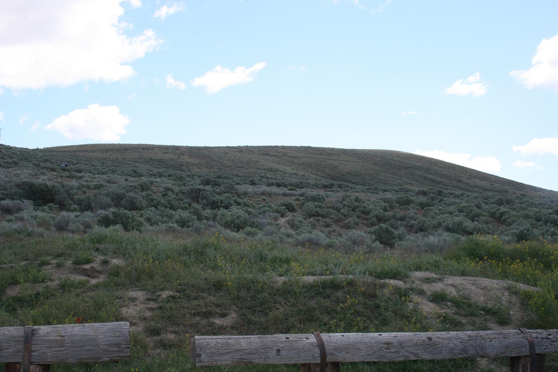Green and grey-green hills covered in brush under a partly cloudy sky.
