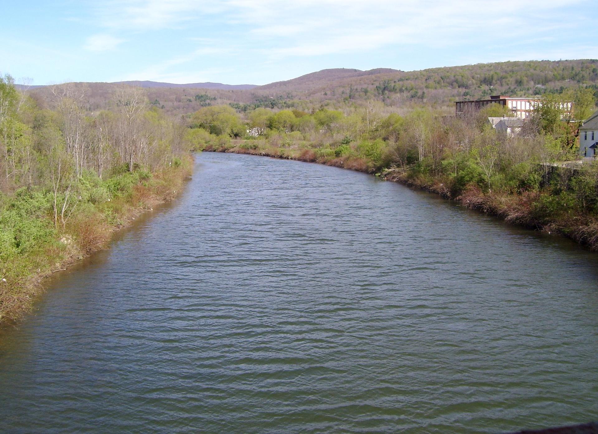 A wide river flows through a valley with tree-covered hills under a bright sky.