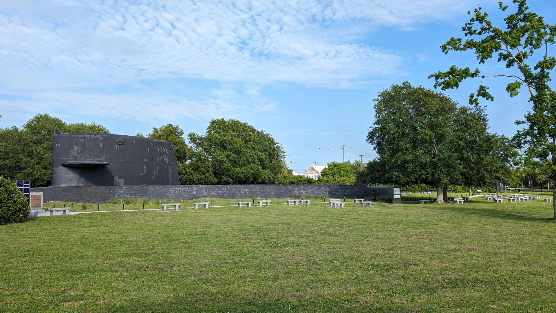Large dark structure in a green park with many benches under a blue sky.