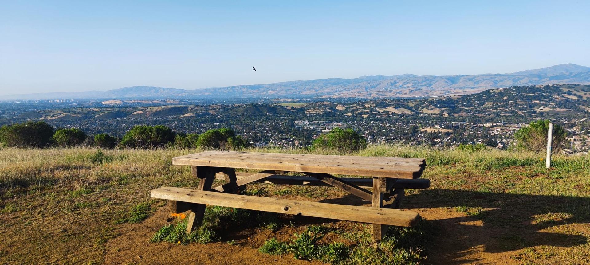 Wooden picnic table on a hilltop overlooking a distant valley and city.