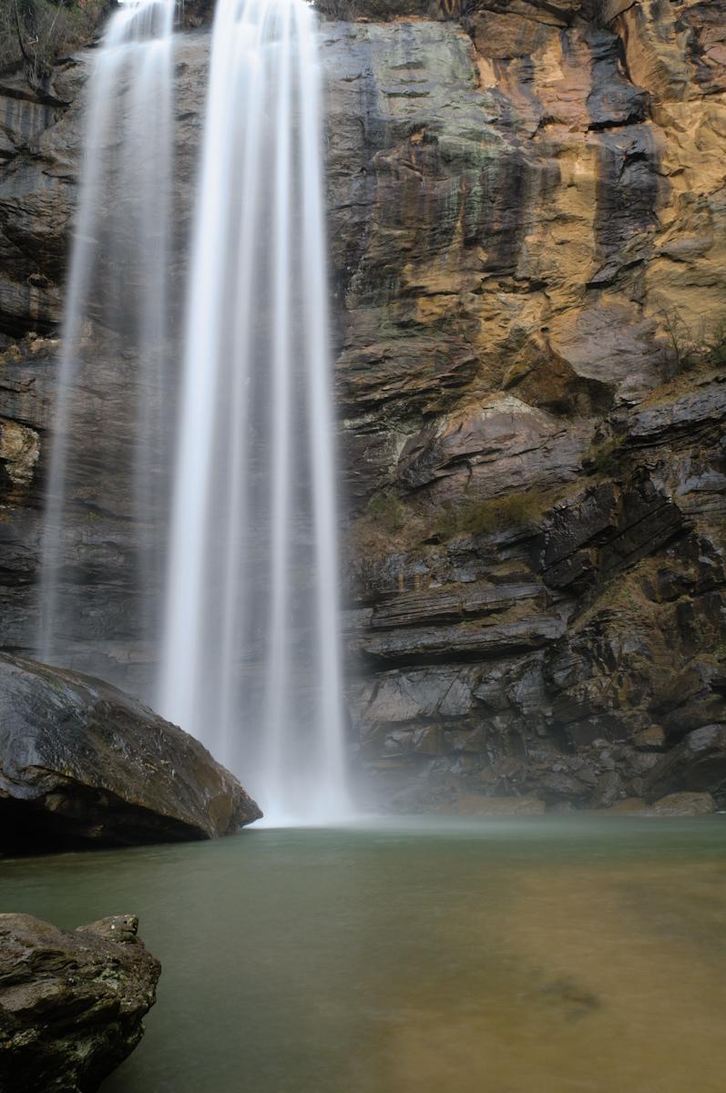 Long exposure captures a waterfall plunging into a serene pool amidst dark rocks.