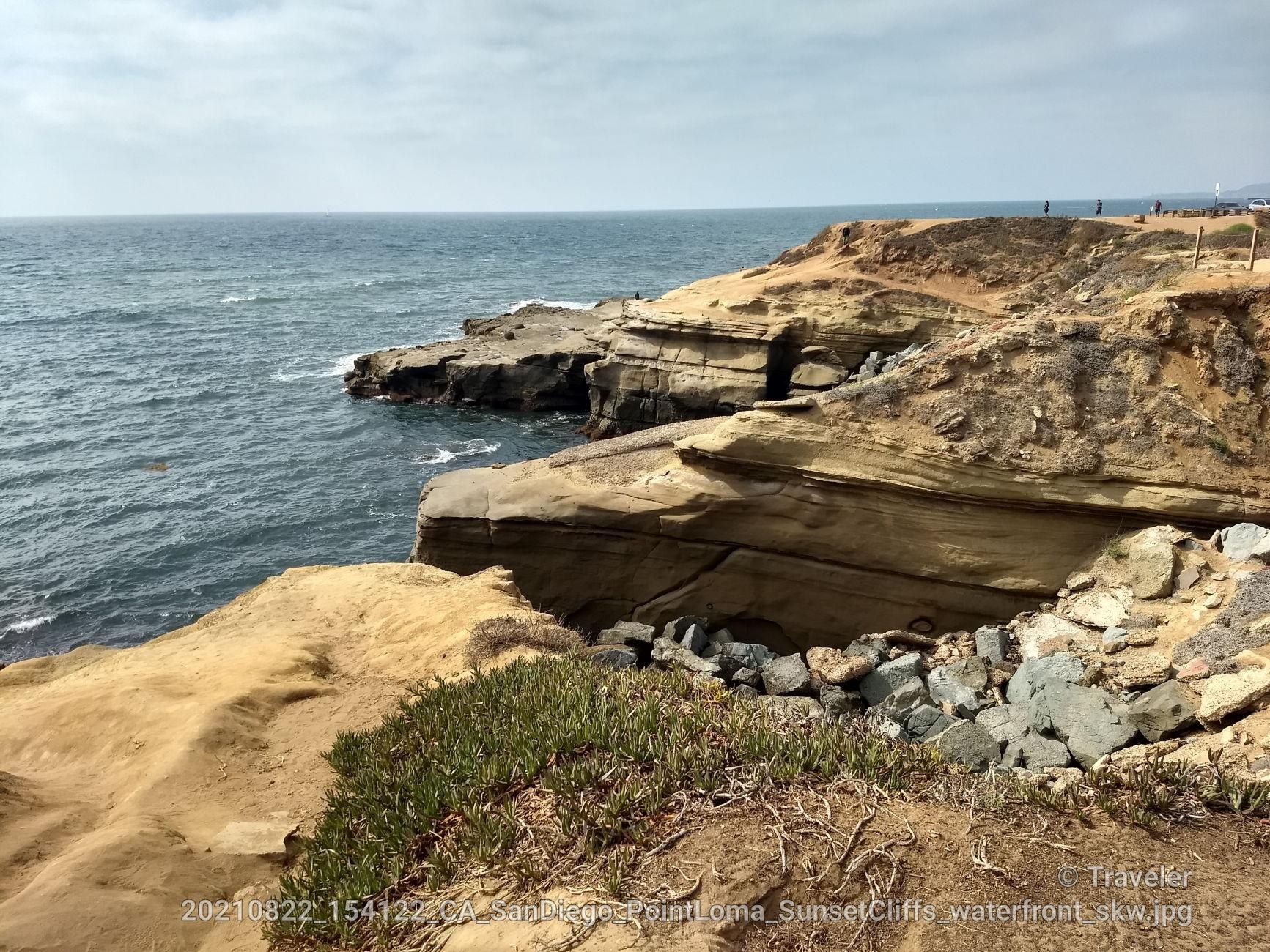 Overcast view of rugged ocean cliffs with distant people. - Sunset Cliffs Coastal Trail