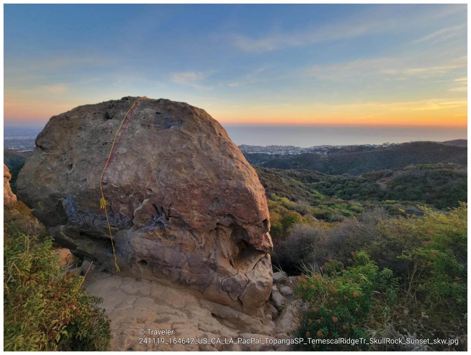 Large rock formation with climbing rope at sunset, ocean in distance.