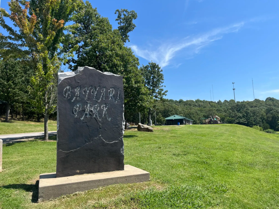Large dark stone sign on a grassy hill under a bright blue sky.