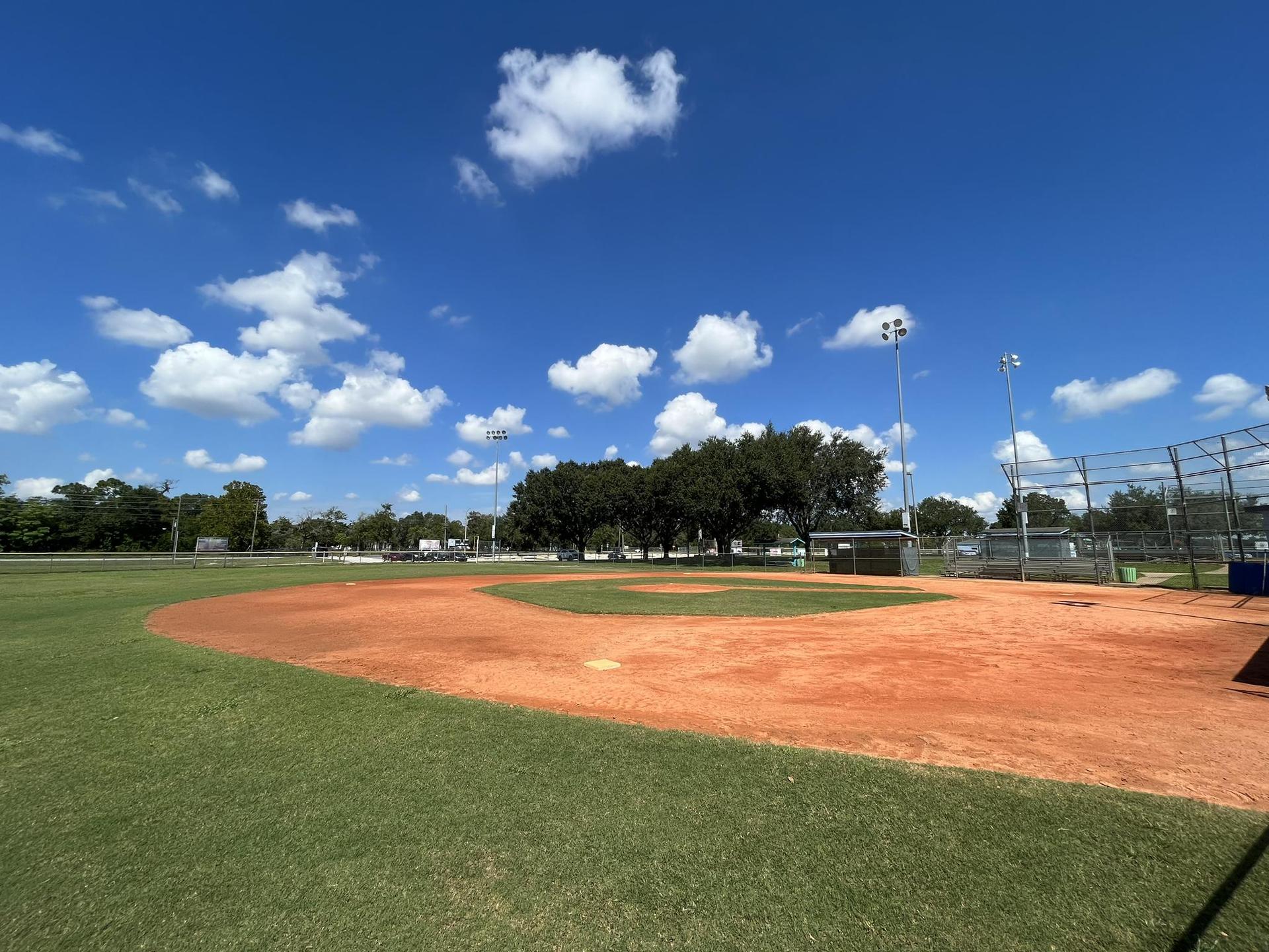 Empty baseball field with red dirt and green grass under a bright blue sky.