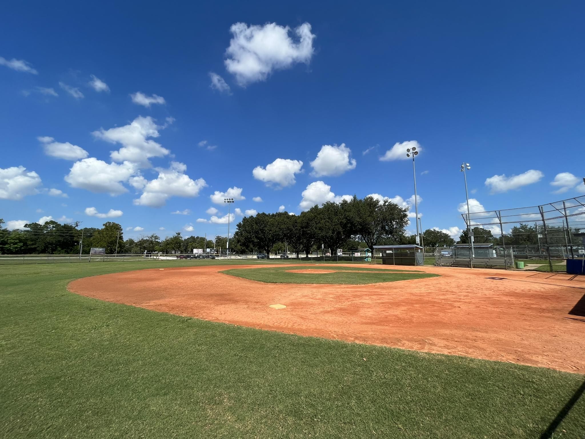 Empty baseball field with red dirt and green grass under a bright blue sky. - Suncoast Trail loop from St. Joan of Arc Catholic Church
