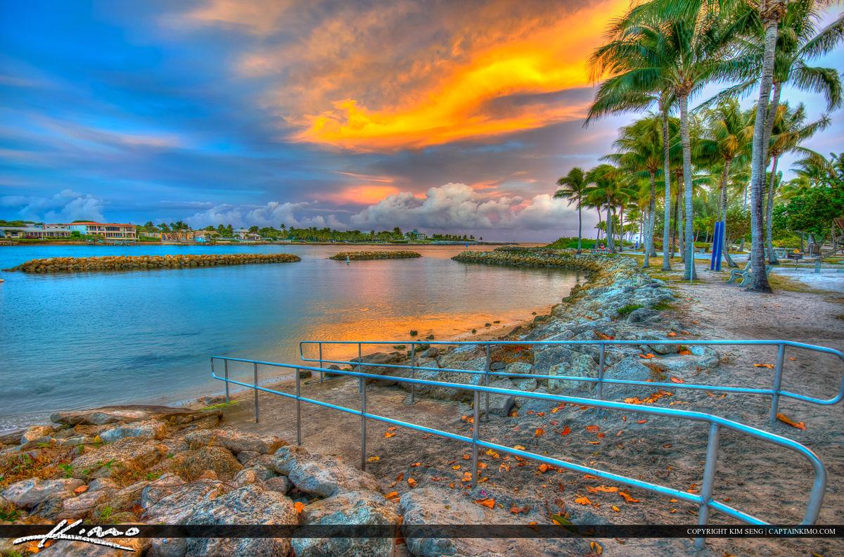 Vibrant sunset over a tropical bay with palm trees and calm water.