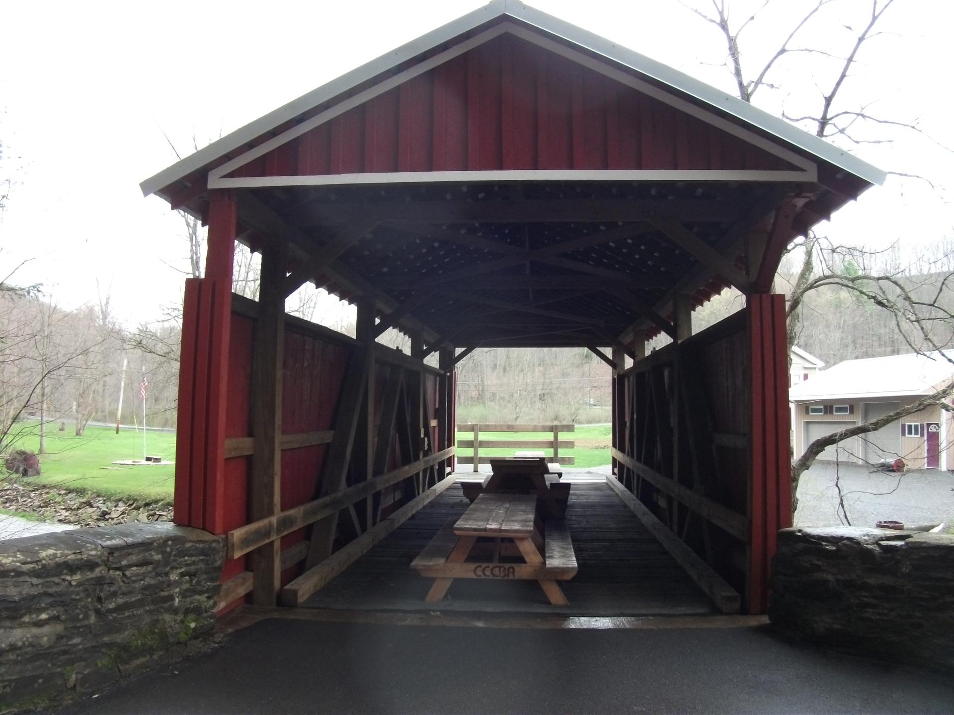 Red covered bridge with a picnic table inside, surrounded by green landscape.
