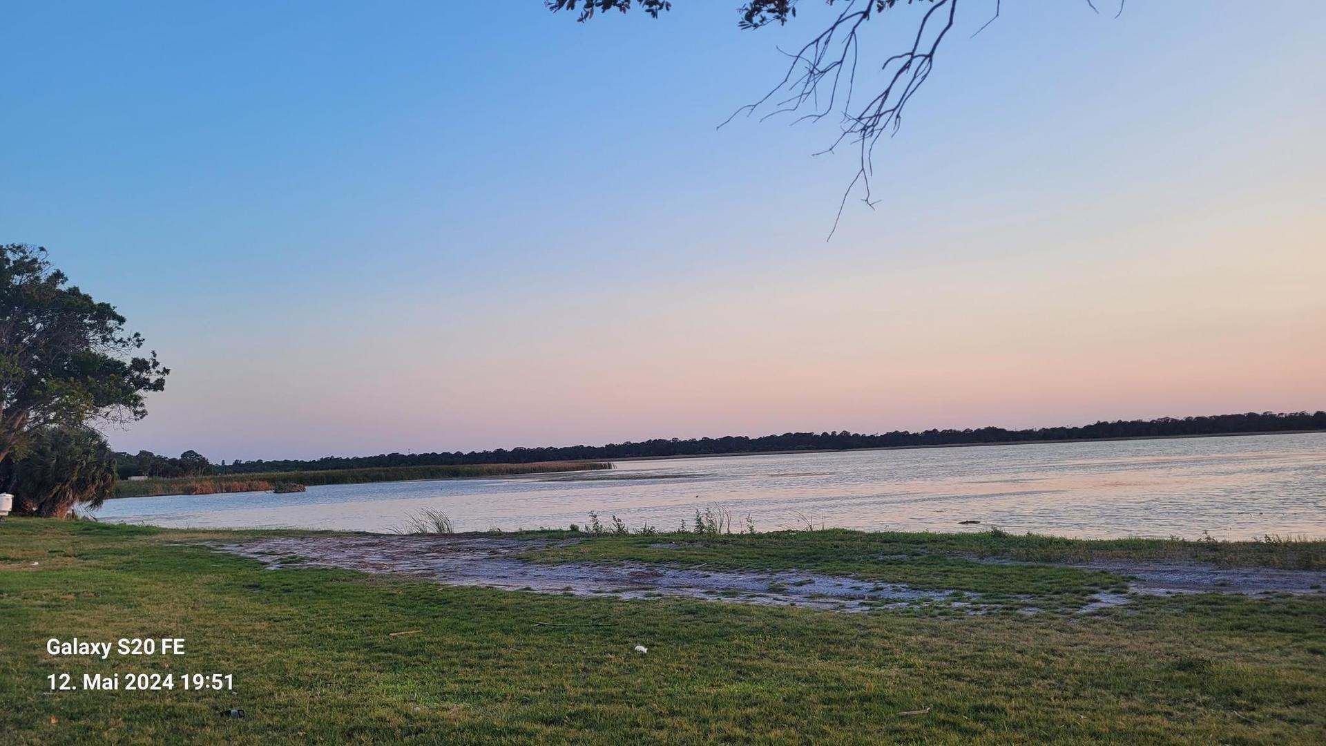 Peaceful lake shore at dusk with a soft, colorful sky.