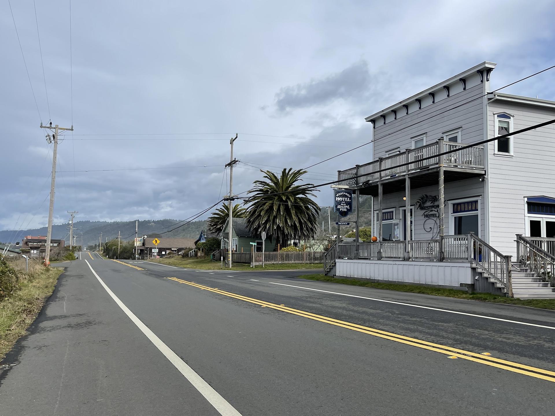 Overcast day, a gray building with a balcony beside a long, empty road.