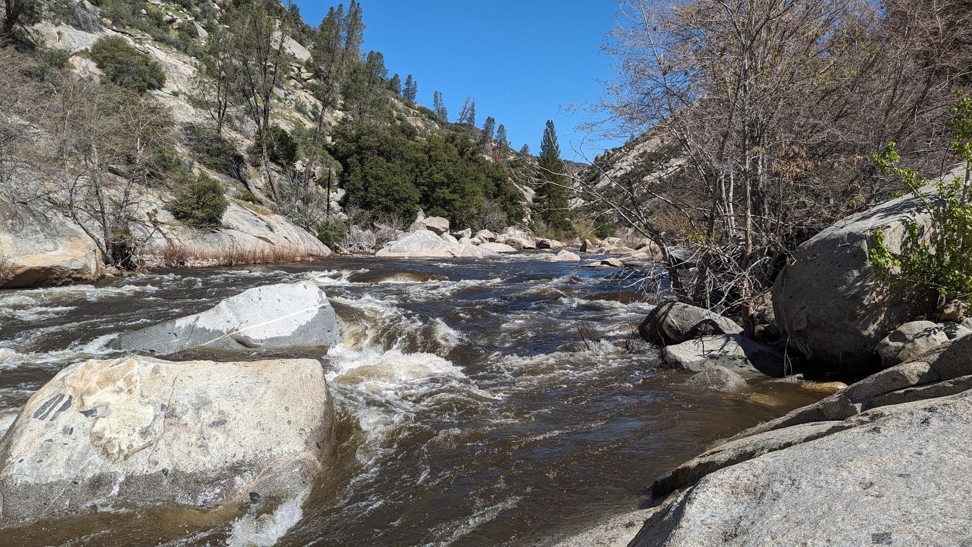 River flowing over rocks in a canyon, surrounded by green hillsides, bright day.
