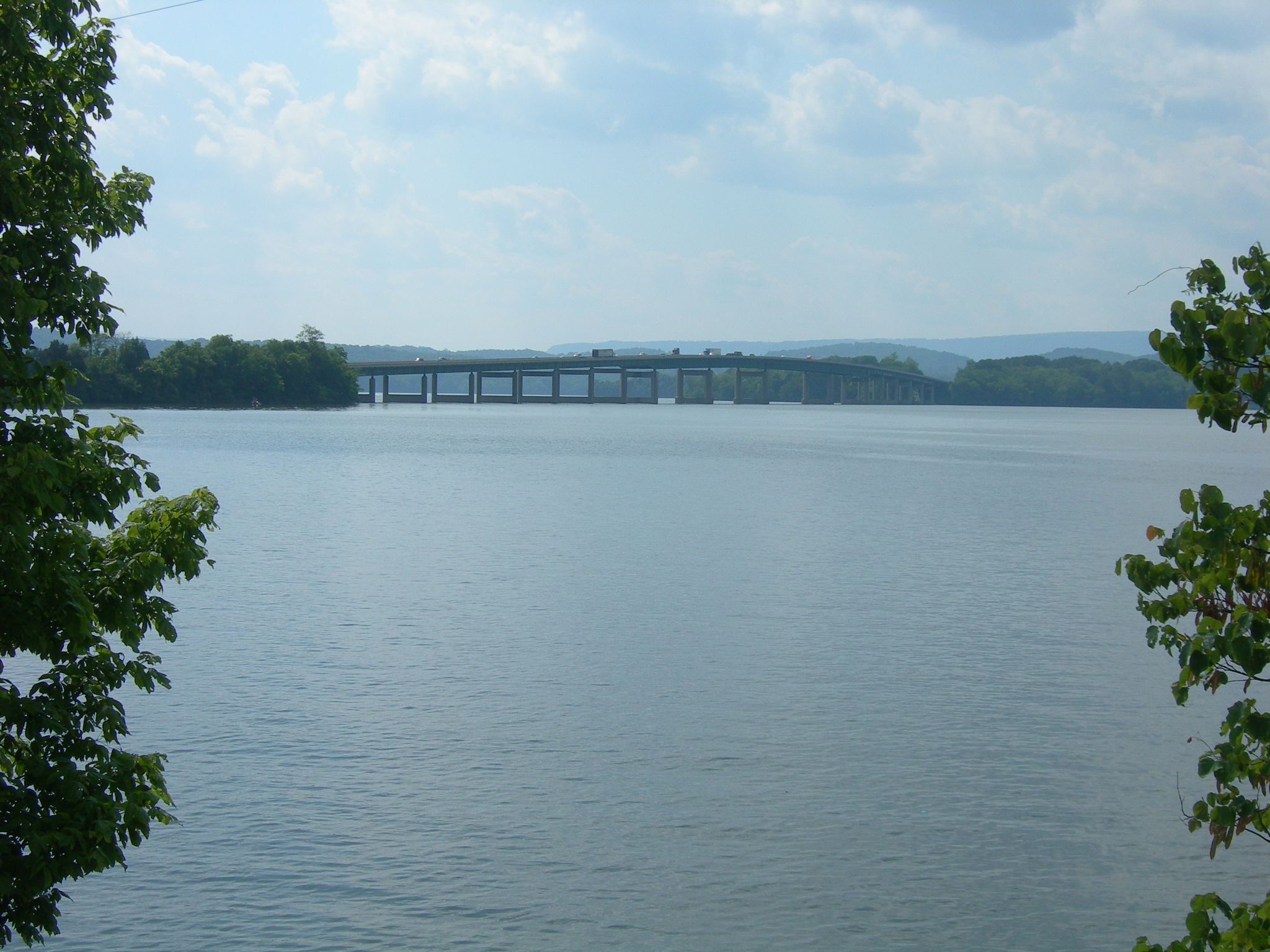 Expansive water with a distant bridge, framed by green trees on a bright day. - Little Cedar Mountain Loop Trail