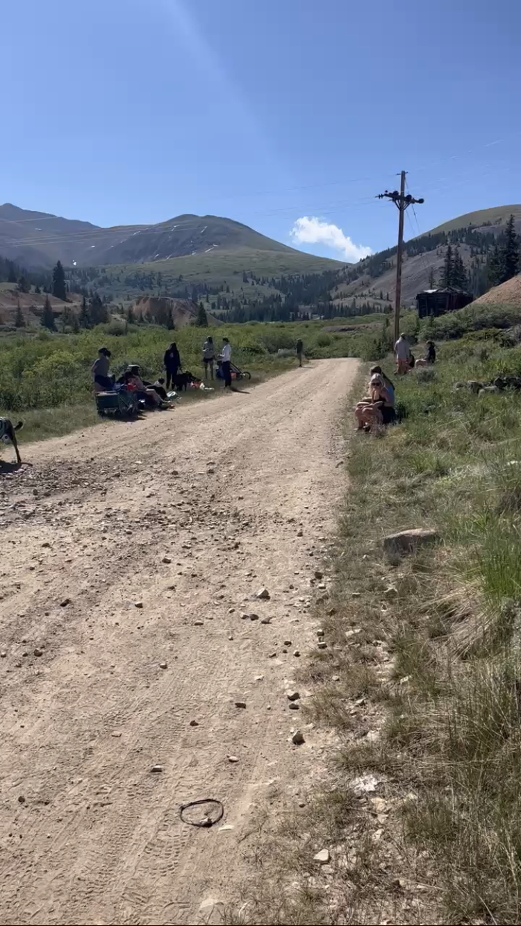 People resting along a dirt road in a sunny mountain landscape.