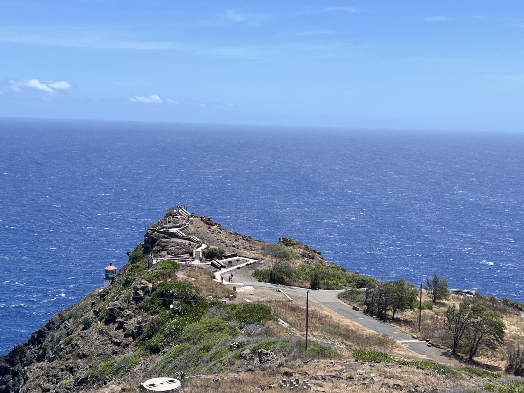 Rocky peninsula with winding paths and structures, surrounded by vast blue ocean.