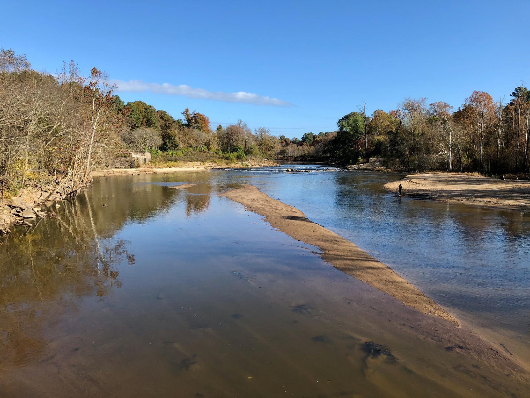 Wide river with a sandbar, surrounded by autumn trees under a clear blue sky.
