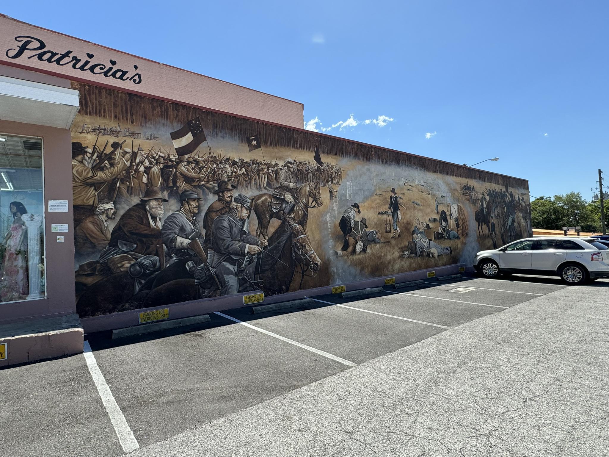 Brightly lit historical mural depicting many figures on a building wall.