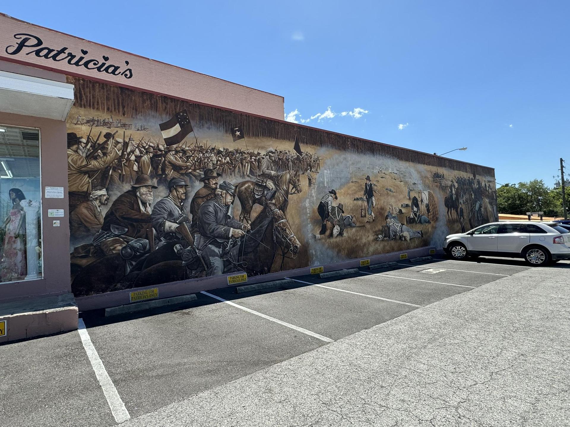 Brightly lit historical mural depicting many figures on a building wall.