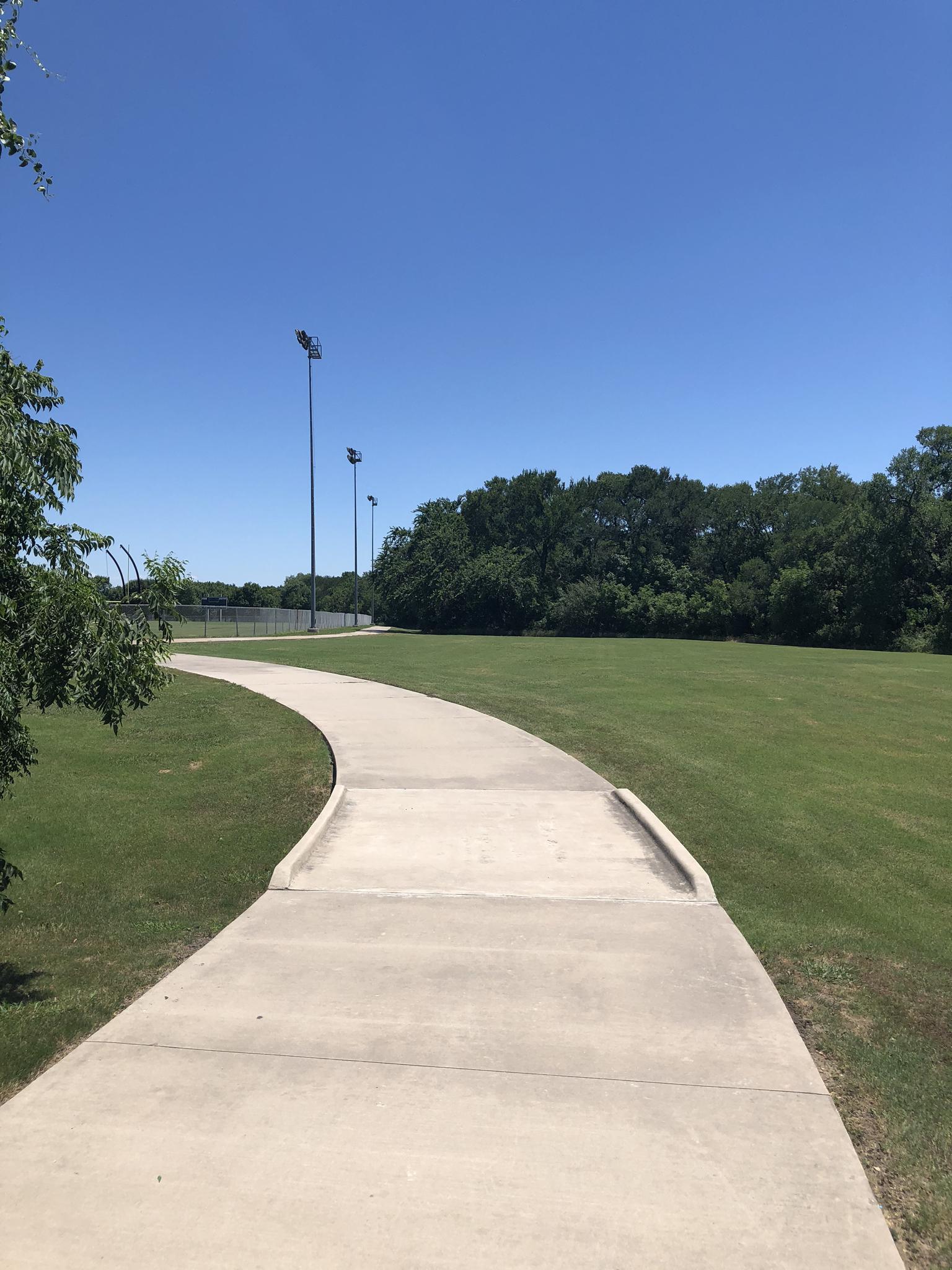 A winding concrete path through green grass under a clear blue sky.