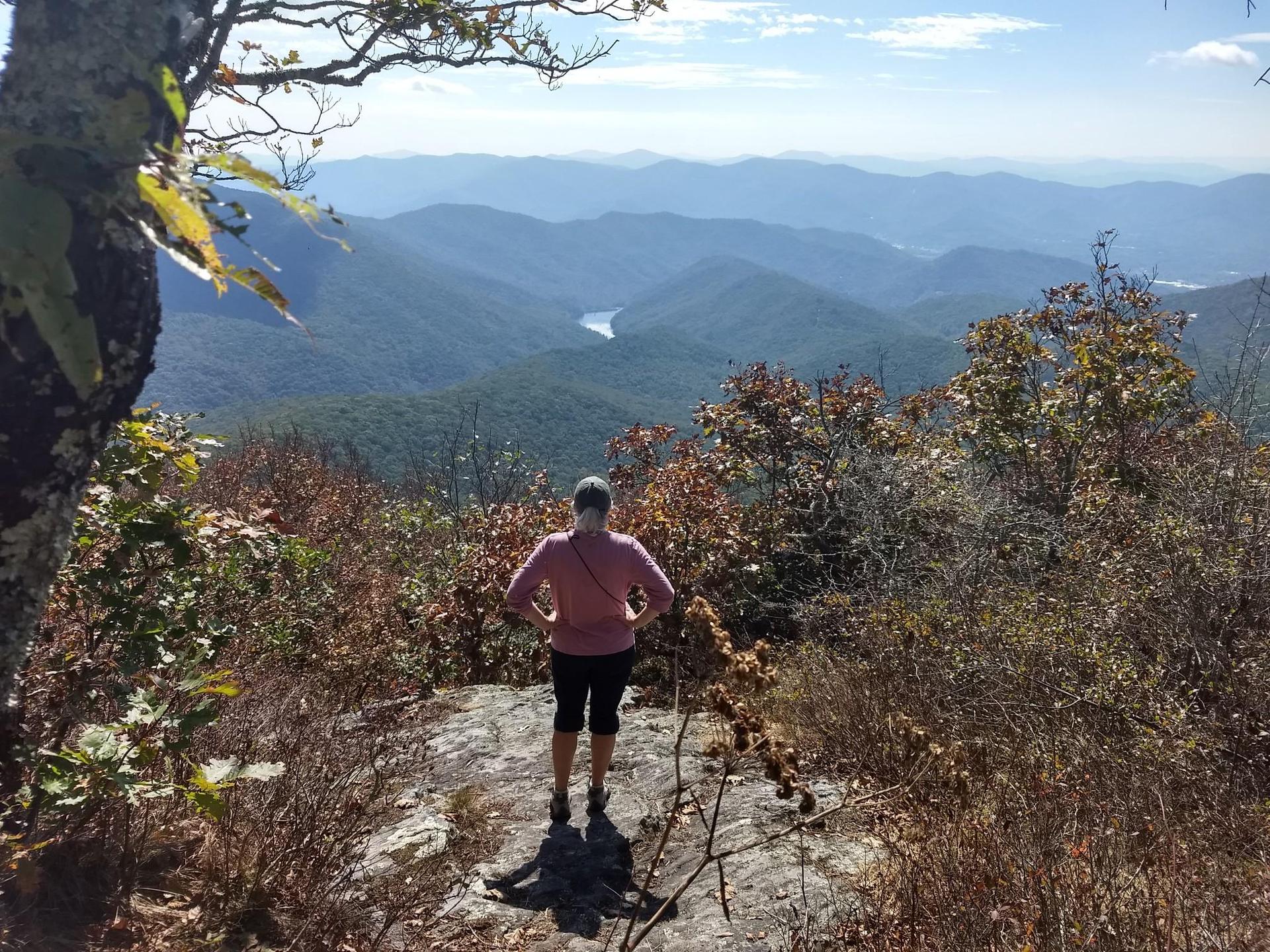 Person views a wide mountain vista with a distant lake on a sunny day.